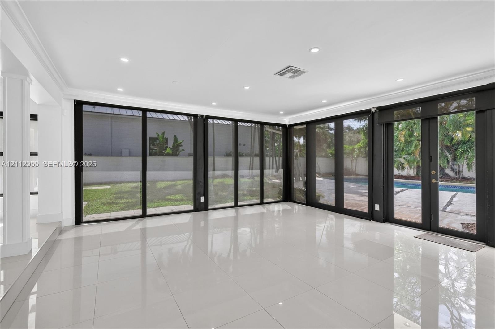 Polished porcelain tile flooring, recessed LED lighting, and expansive floor-to-ceiling black-framed glass wall panels opening to a rear exterior pati