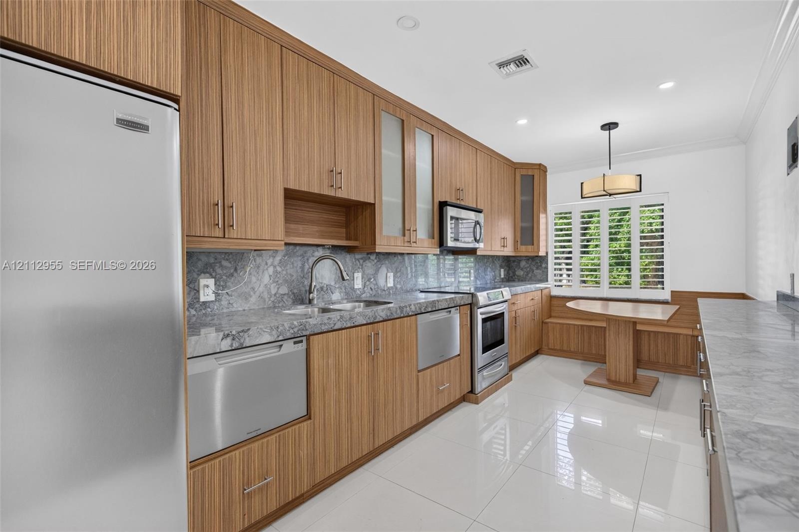 Kitchen featuring wood-grain cabinetry, stone countertops with matching backsplash, stainless steel appliances, polished tile flooring, and a built-in