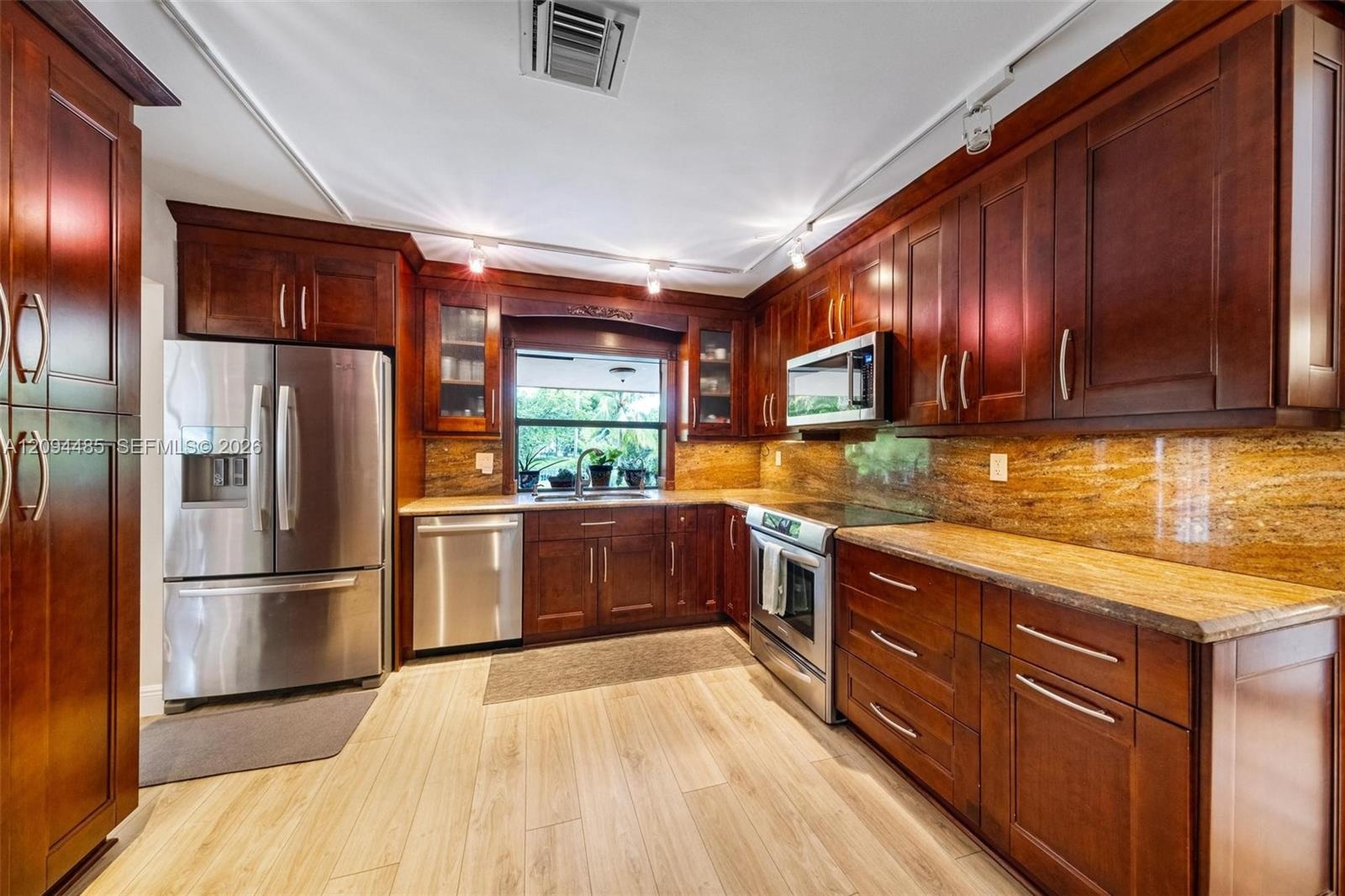 Kitchen featuring custom stained wood cabinetry, stone countertops, integrated stainless steel appliances, and wood-finish flooring