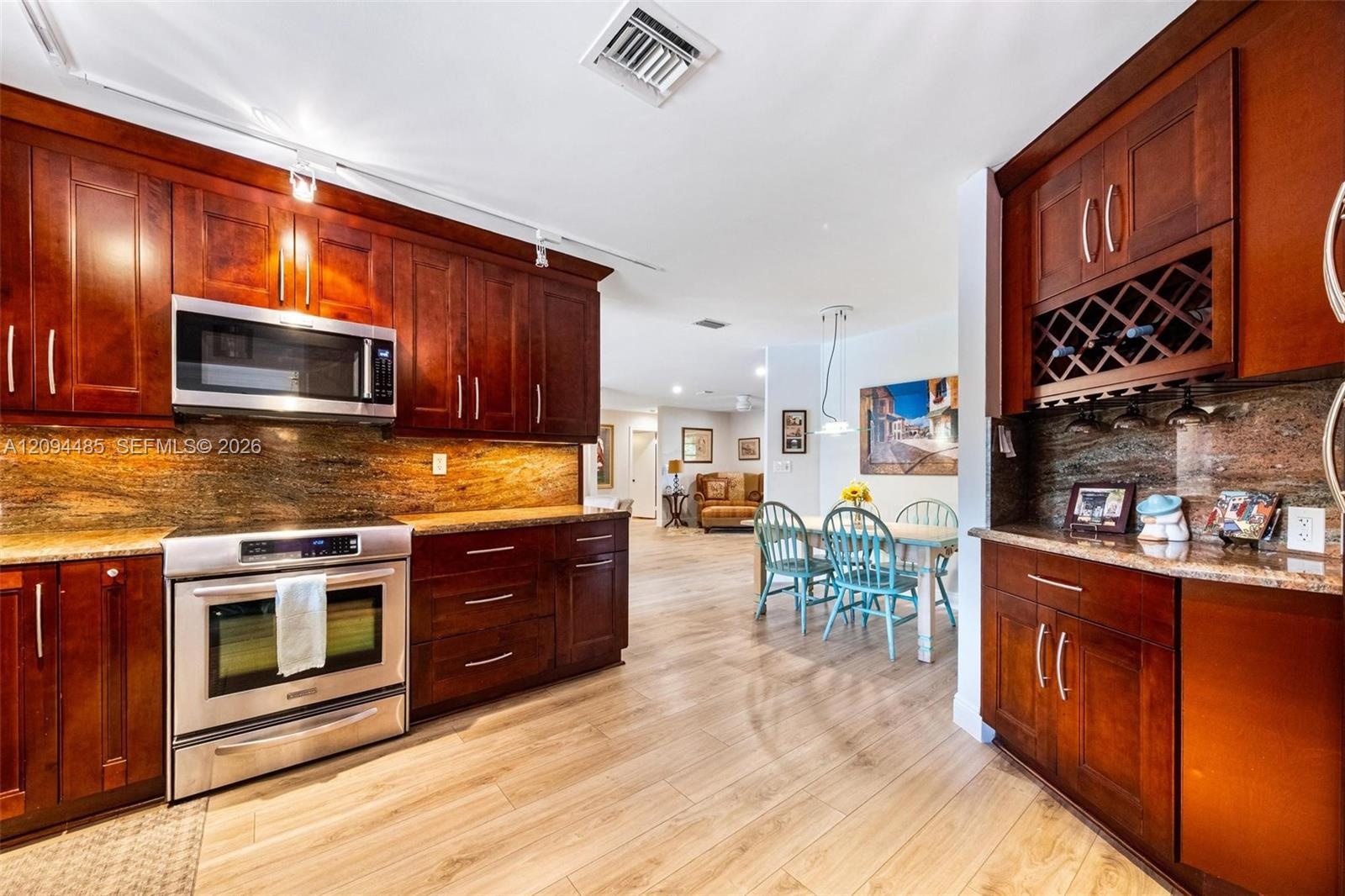 Kitchen featuring rich-toned wood cabinetry, stone countertops, stainless steel appliances, built-in wine rack, and light wood-finish flooring