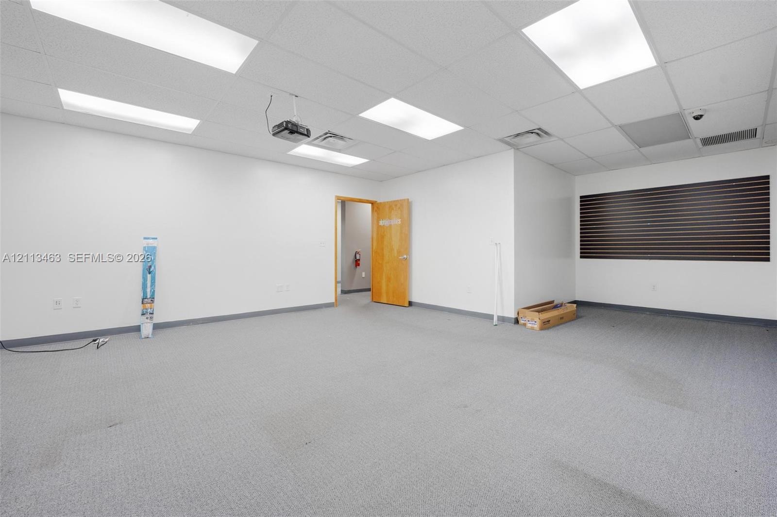 Interior space featuring recessed drop-ceiling lighting, carpeting, a wood-finish interior door, and a horizontal slatted wall accent