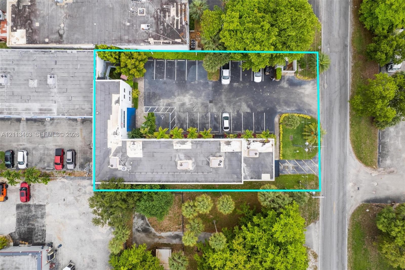 Aerial perspective of the property featuring a paved asphalt parking area, designated parking stalls, mature perimeter landscaping, and established tr