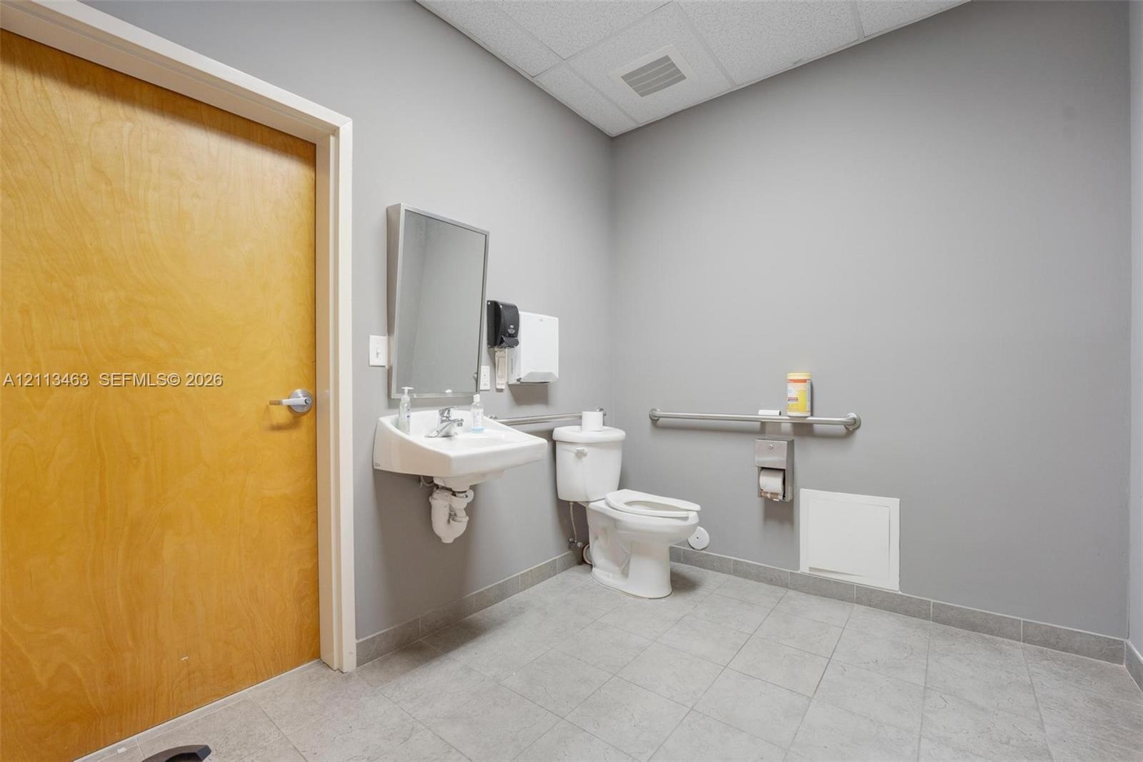 Wall-mounted sink, flat-panel wood-finish door, tile flooring, and metallic grab bars