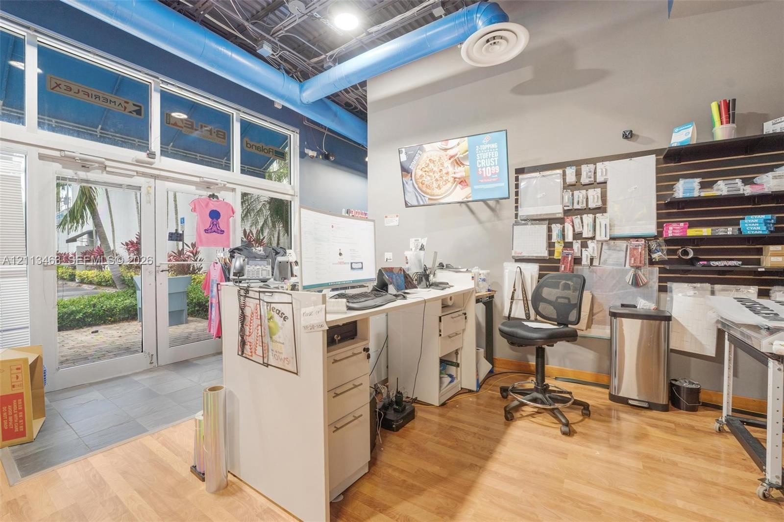 Commercial space featuring wood-finish flooring, floor-to-ceiling glass panel entry doors, exposed industrial-style ceiling with blue ductwork, and bu