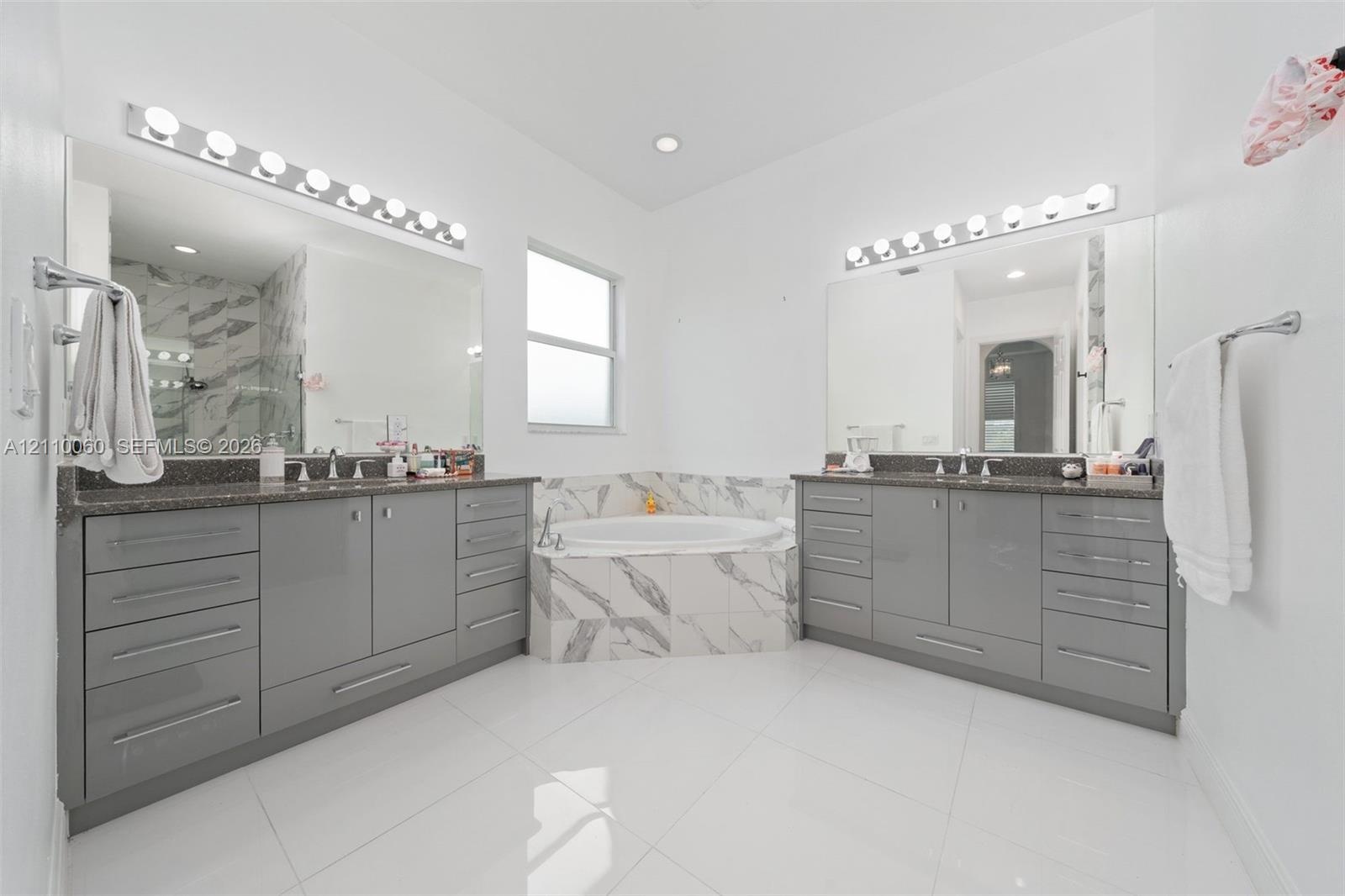 Dual vanities featuring gloss-finish cabinetry, stone countertops, integrated basins, and polished hardware, complemented by a tiled soaking tub and p