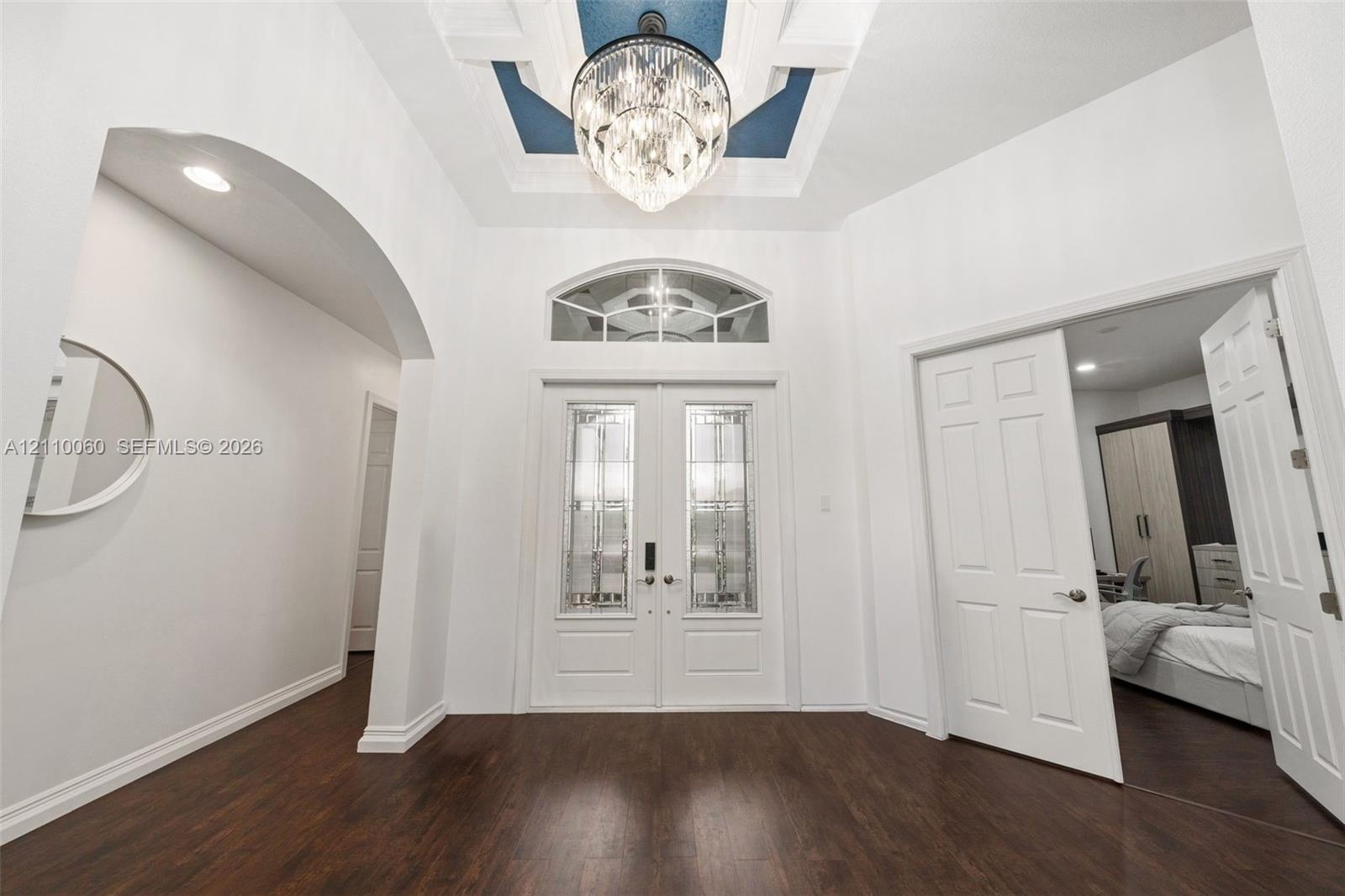 Foyer featuring double entry doors with decorative glass inserts, a recessed tray ceiling with accent color, a crystal chandelier, arched architectura