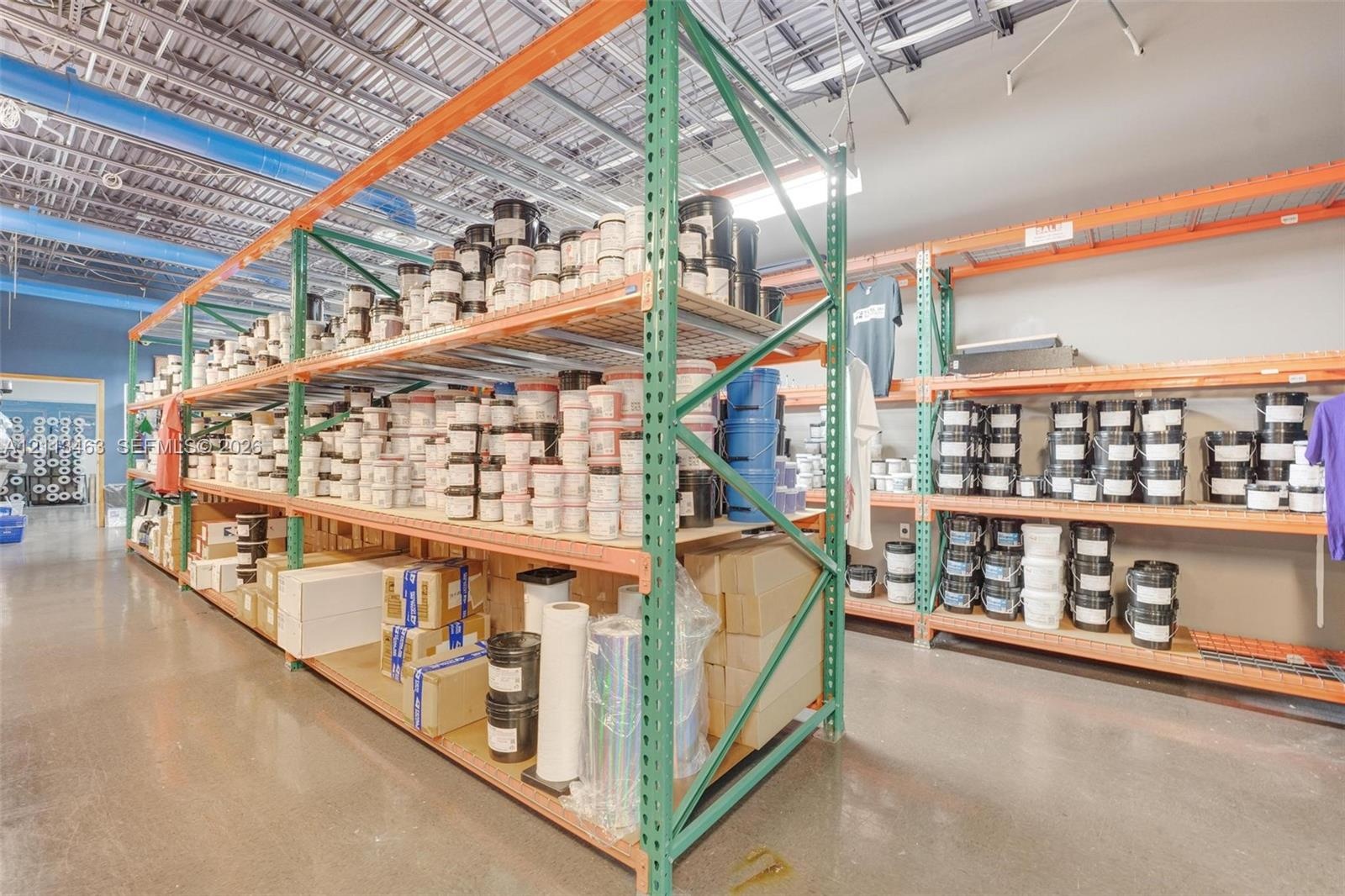 Industrial storage space featuring high-clearance ceilings, exposed structural metal framing, polished concrete flooring, and heavy-duty steel shelvin