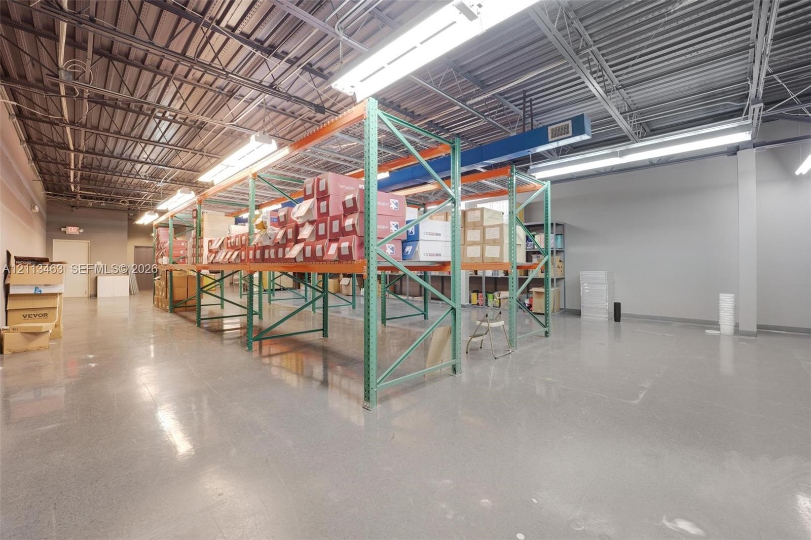 Industrial warehouse interior featuring polished concrete flooring, exposed high-ceiling steel framing, integrated industrial shelving units, and line