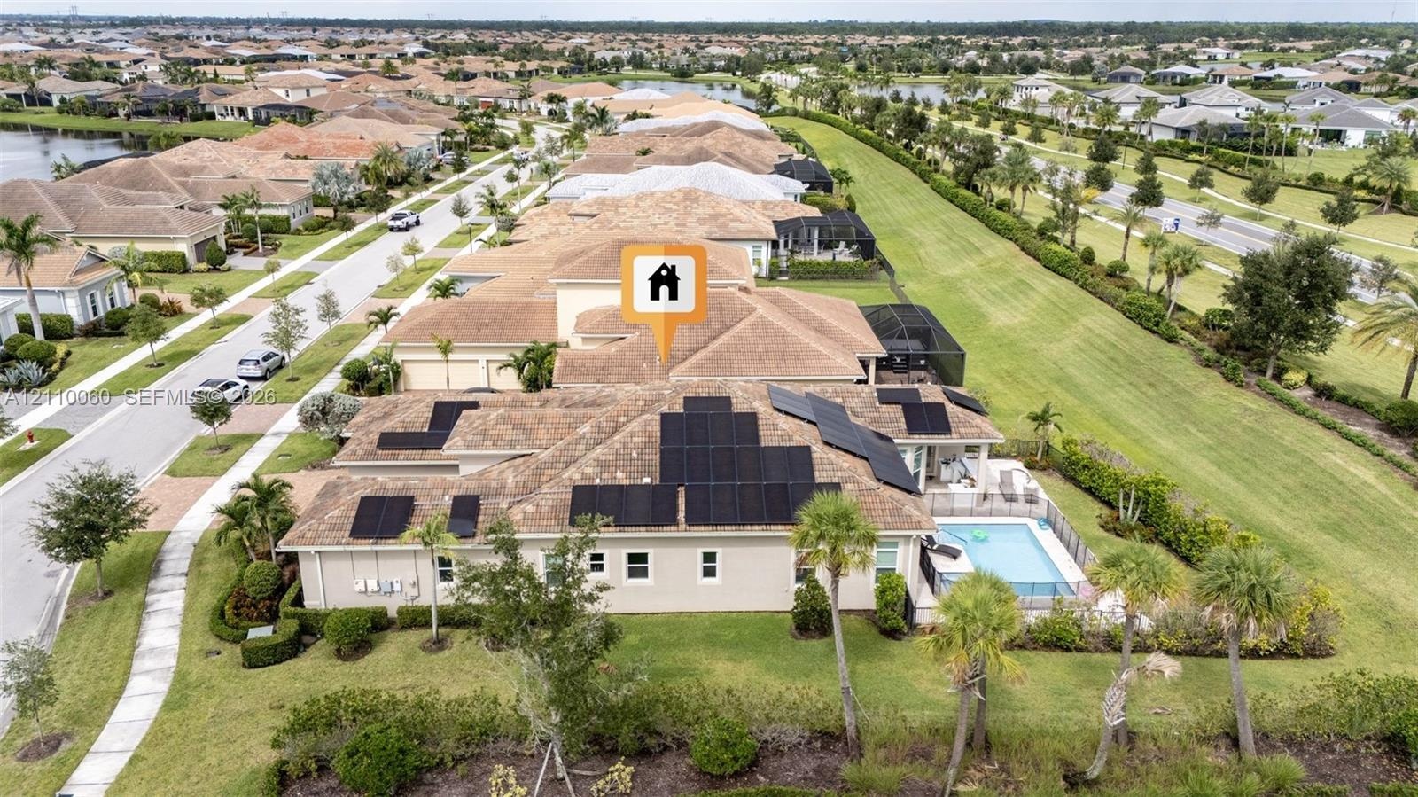 Aerial perspective featuring a tile-roof residence with integrated solar panel arrays, a screened-in swimming pool, and an expansive lawn