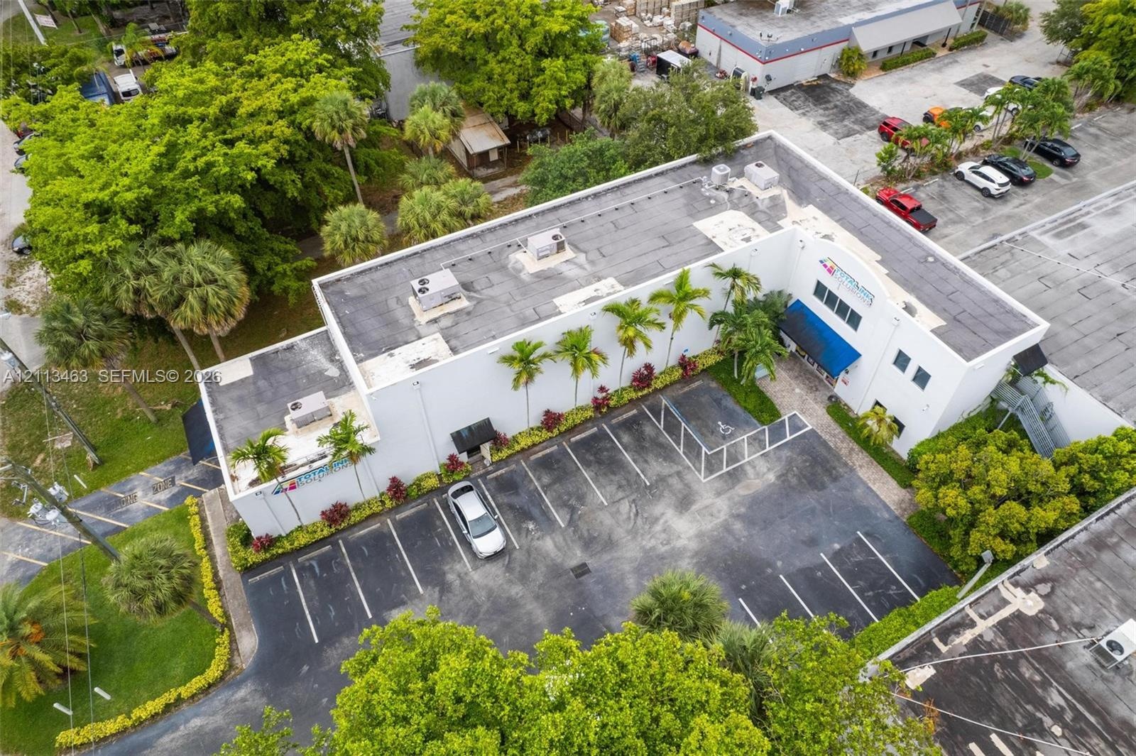 Commercial property featuring an exterior parking area, multiple rooftop HVAC units, established perimeter landscaping, and asphalt paving