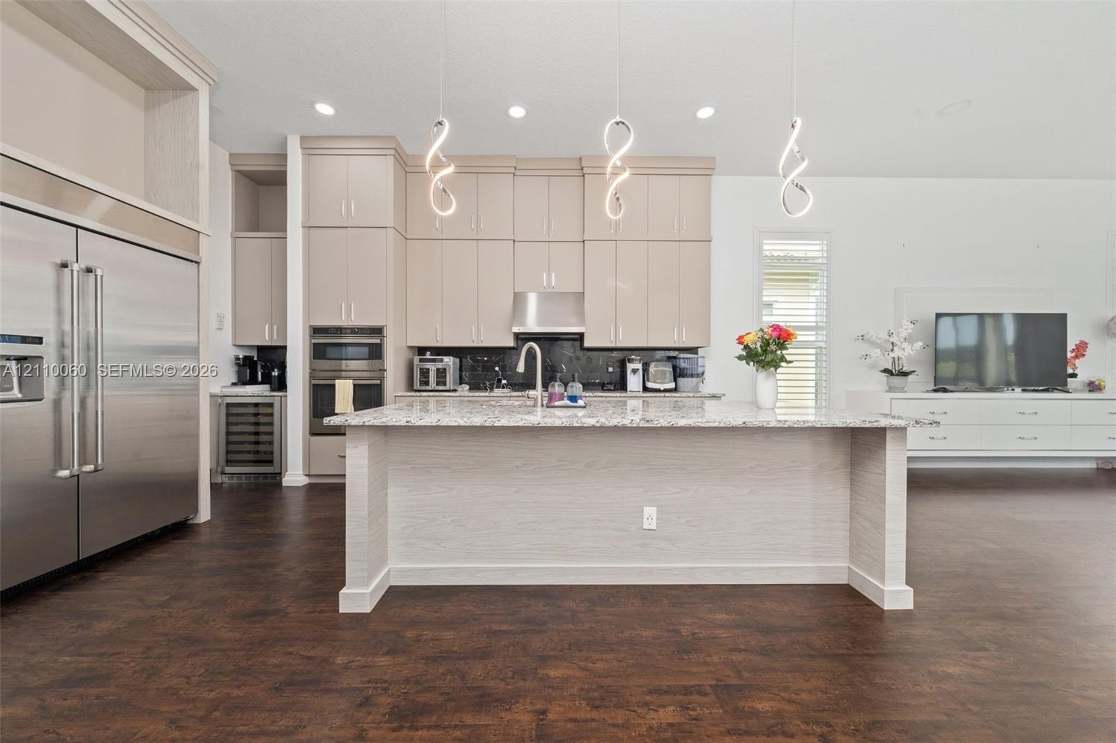 Kitchen featuring floor-to-ceiling cabinetry, a central island with stone countertop, stainless steel double wall ovens, built-in wine refrigeration, 