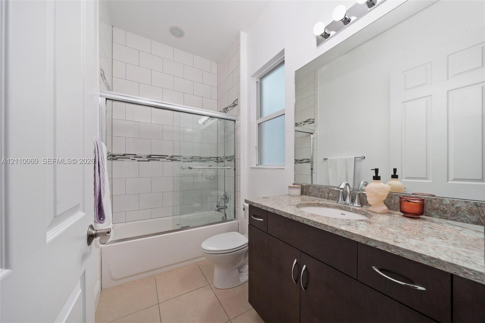 Bathroom featuring dark wood-finish cabinetry, a stone-patterned countertop, an integrated sink, a full-width vanity mirror, and a tub-shower combinat