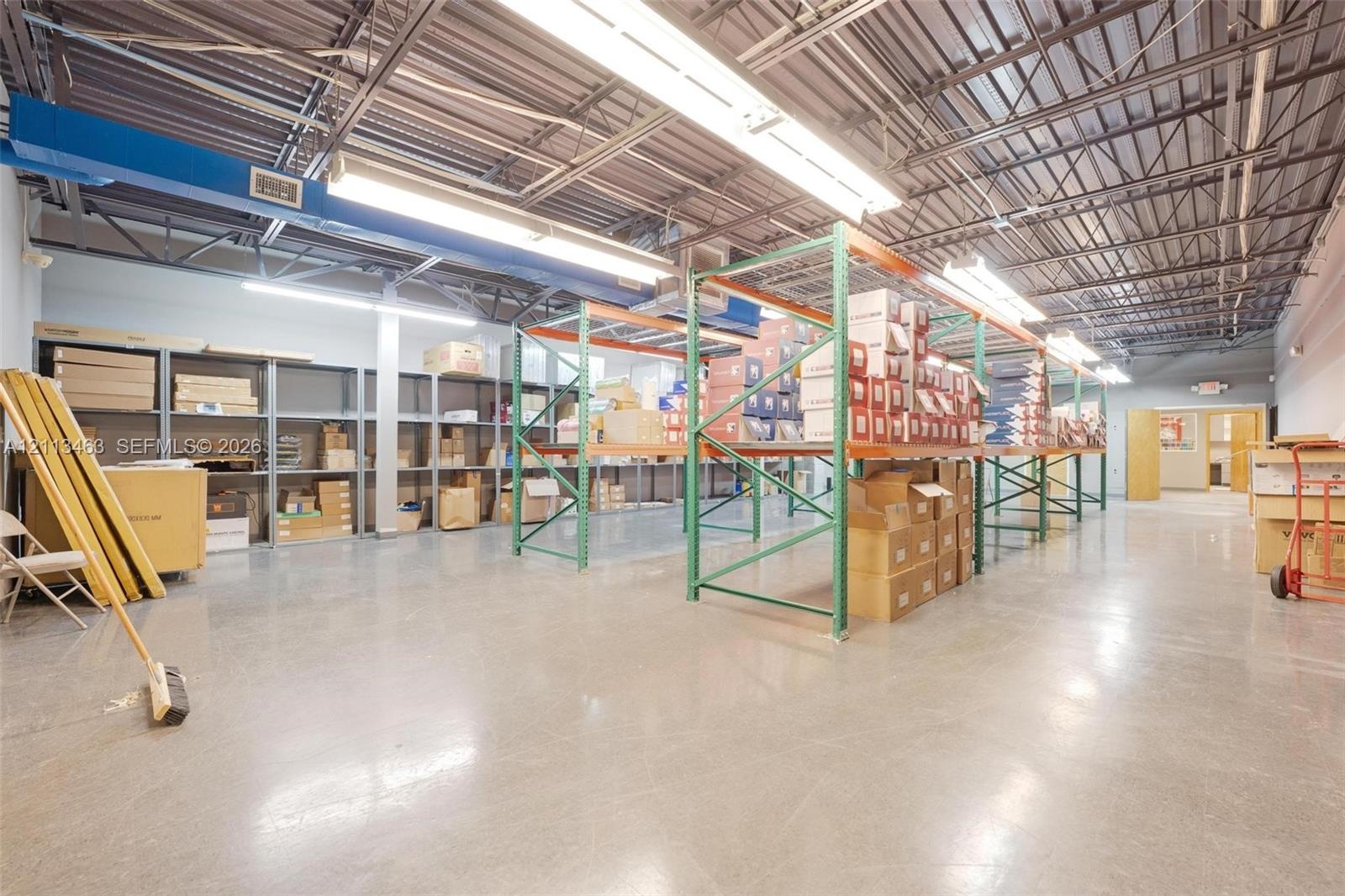 Expansive industrial space featuring polished concrete flooring, open-truss ceiling, high-output linear fluorescent lighting, and integrated metal she
