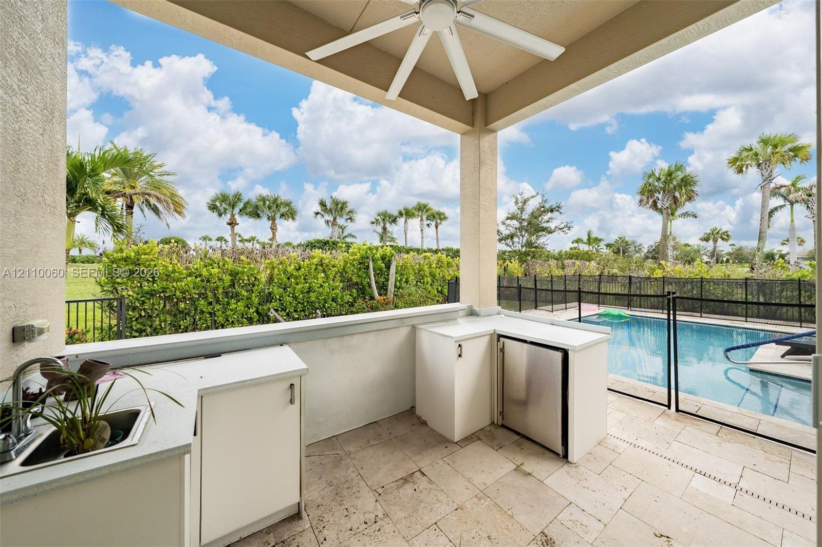 Covered outdoor kitchen featuring light-toned cabinetry, solid surface countertops, stainless steel refrigeration, and a sink, complete with stone-til