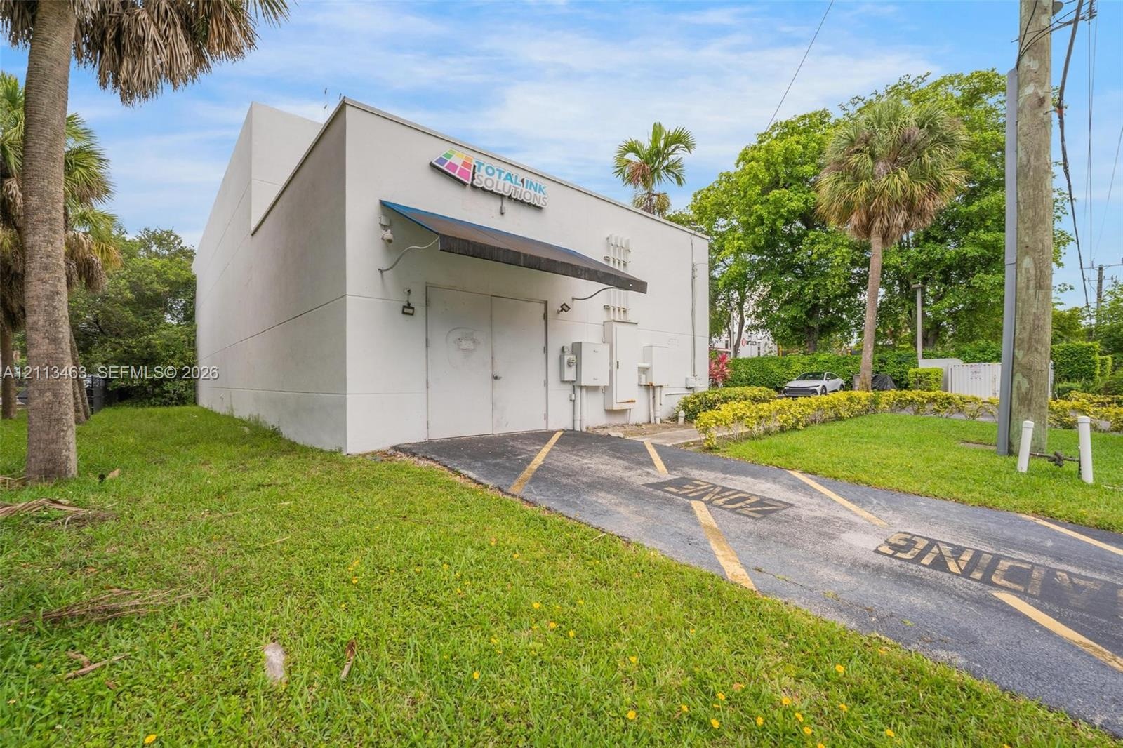 Commercial exterior featuring a smooth-finish facade, metal awning, double-door entrance, and dedicated paved loading zone