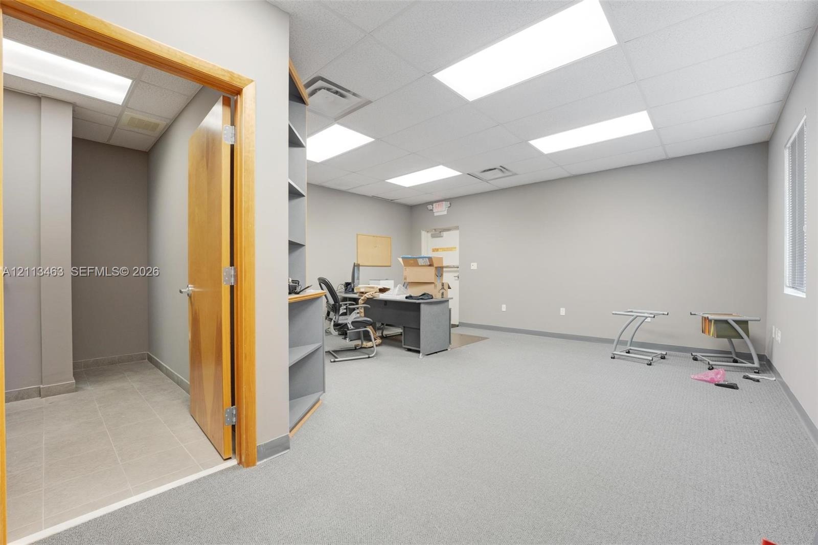 Interior workspace featuring recessed ceiling lighting, wall-to-wall carpeting, built-in shelving, and a secondary room finished with tile flooring