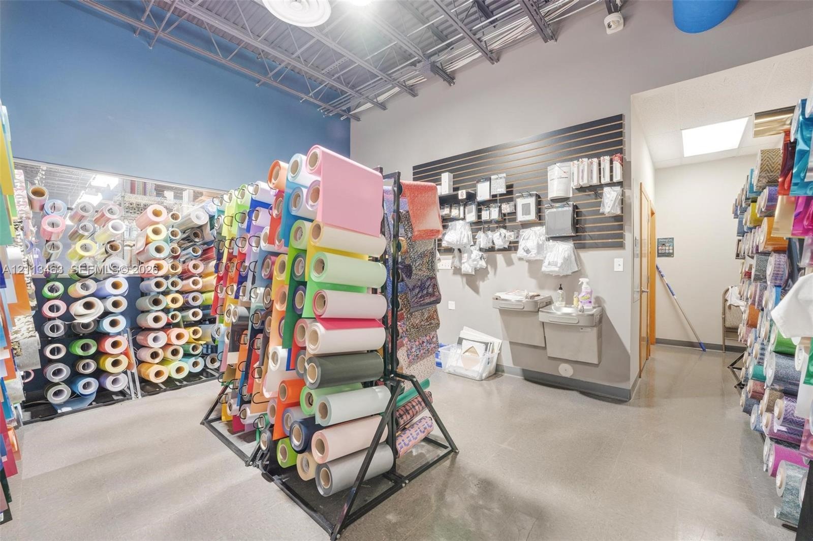 Commercial space featuring industrial exposed ceiling, slat wall storage system, smooth flooring, and wall-mounted water fountain
