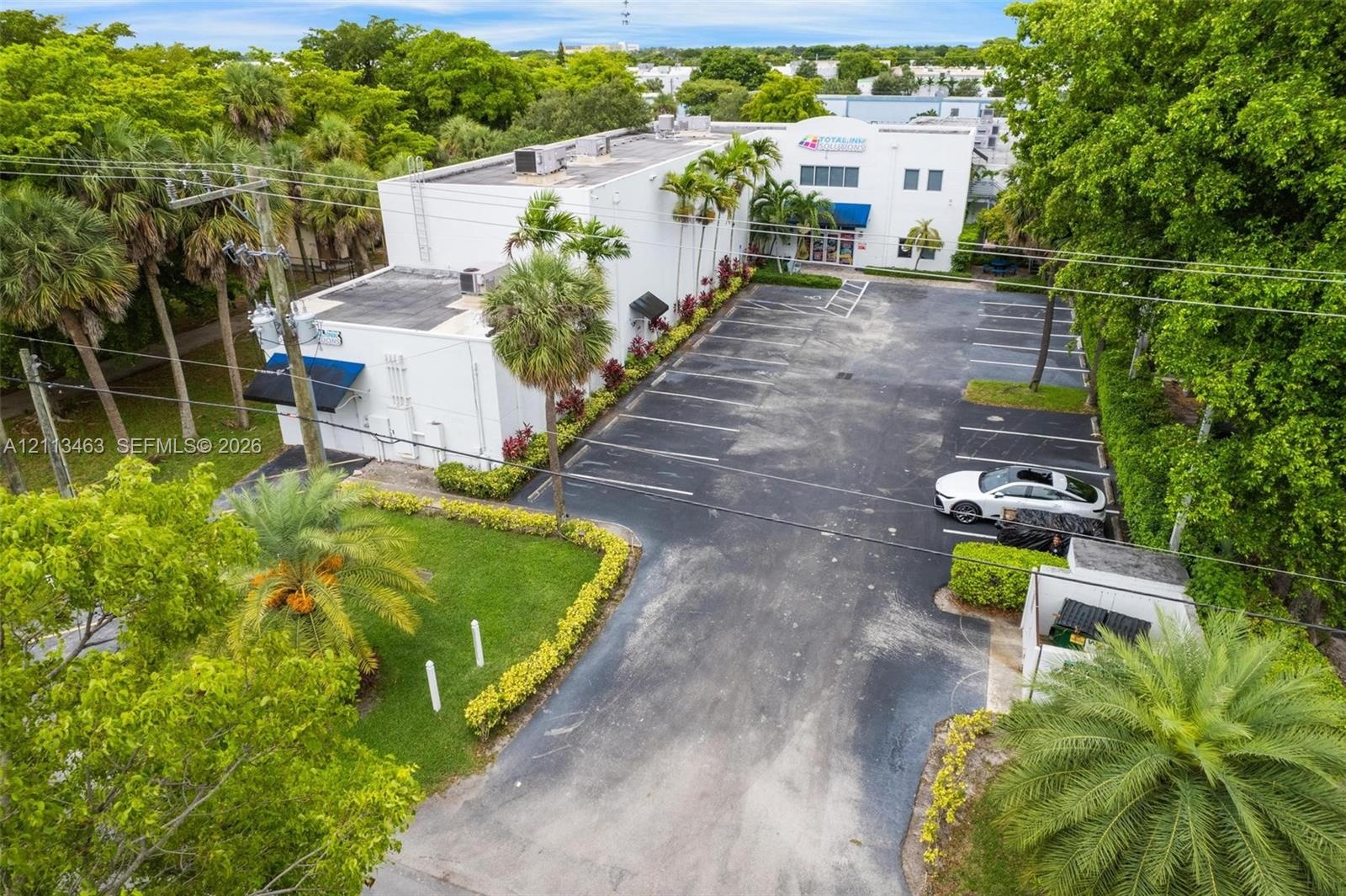 Multi-story commercial building featuring a dedicated asphalt parking lot, manicured lawn areas, established palm trees, and perimeter landscaping