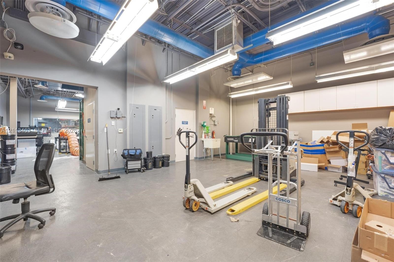 Industrial space featuring high ceilings with exposed ductwork, fluorescent lighting, concrete flooring, and built-in upper cabinetry