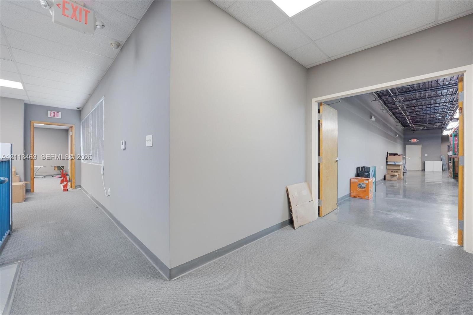 Commercial interior featuring neutral-toned walls, industrial-style exposed ceiling beams, polished concrete flooring, drop ceiling panels, and wood-v