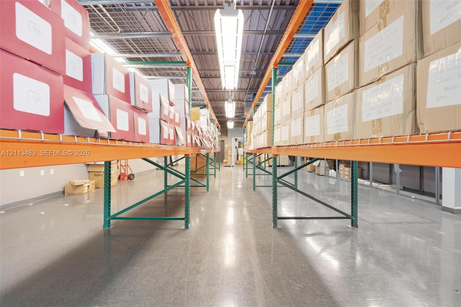 Industrial warehouse space featuring polished concrete flooring, exposed corrugated metal ceiling, high-output linear fluorescent lighting, and extens