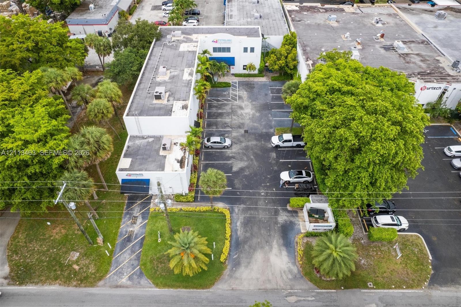 Commercial property featuring a multi-level structure, paved surface parking lot, professional landscaping, and mature palm trees