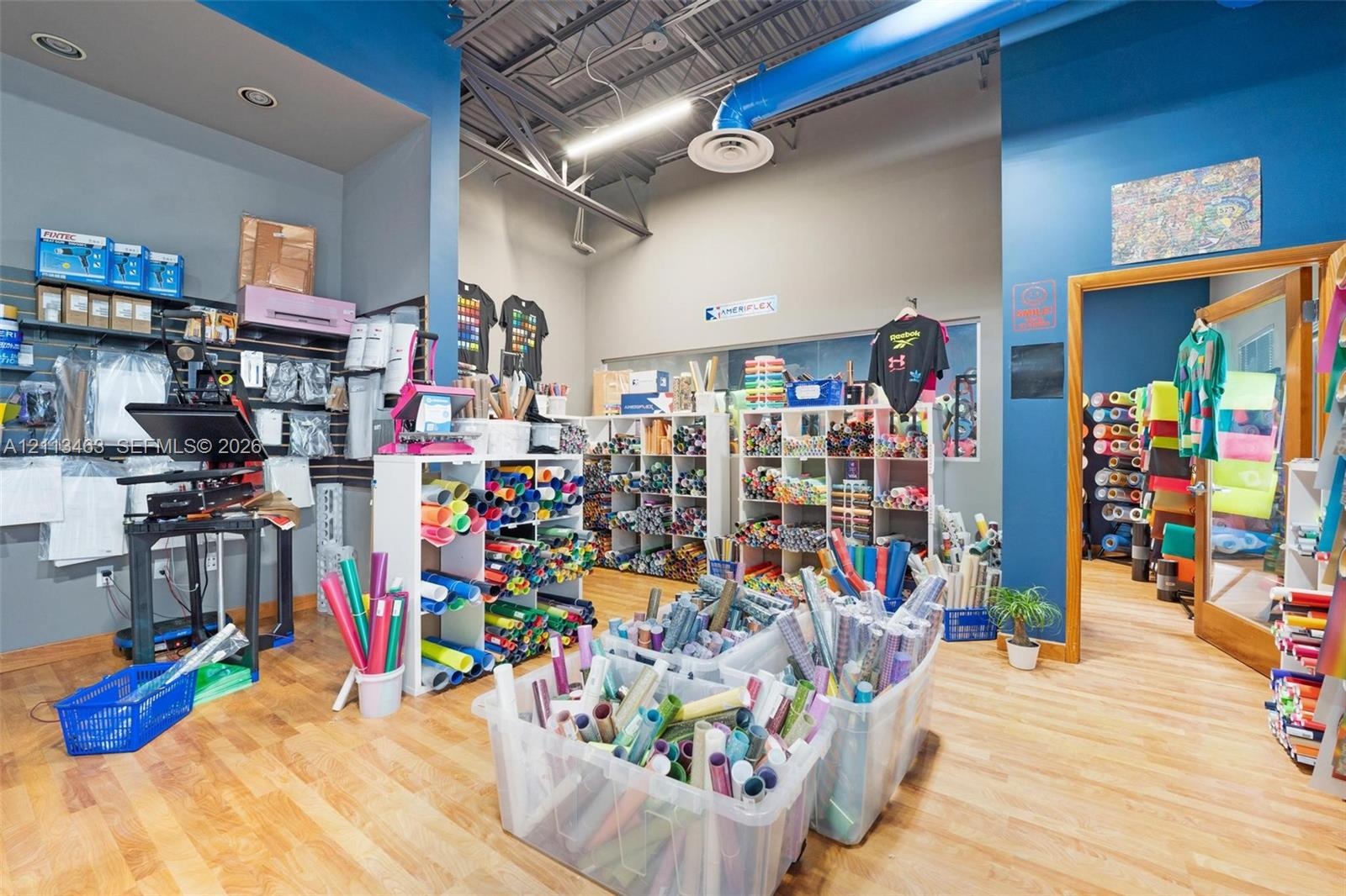 Open-concept interior space featuring exposed industrial-style ceiling ductwork, wood-finish flooring, recessed lighting, and wall-mounted grid shelvi