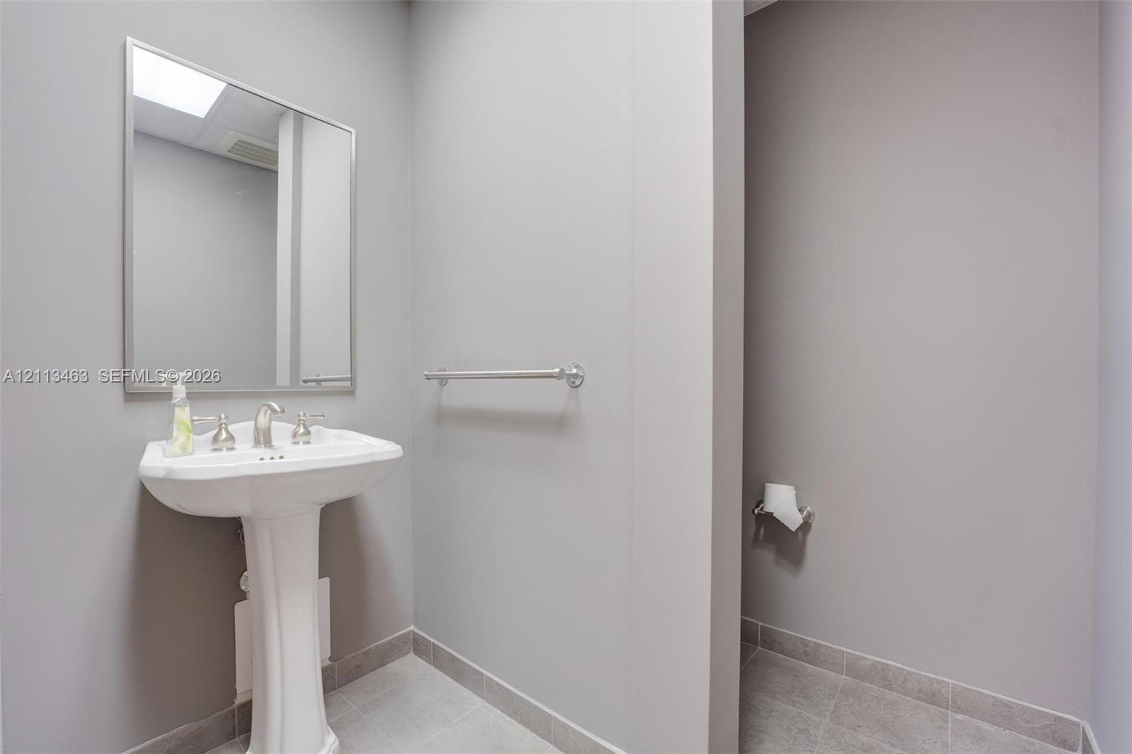 White pedestal sink featuring a metallic faucet, framed wall-mounted mirror, and horizontal towel bar finished in coordinating metallic hardware, set 