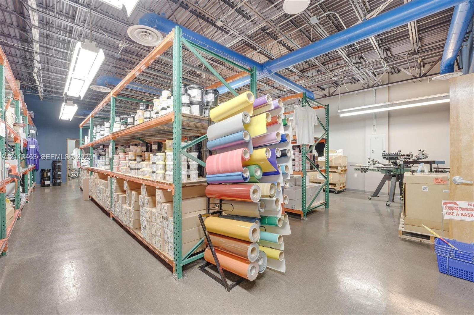 Industrial workspace featuring high-clearance ceilings with exposed ductwork, concrete flooring, overhead linear lighting, and heavy-duty steel pallet