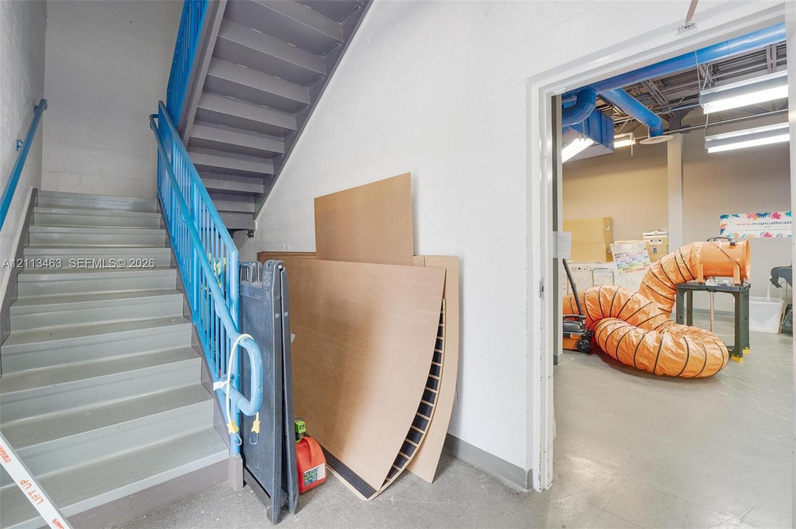Interior stairwell featuring painted metal stairs, blue steel handrails, and exposed ceiling infrastructure with linear lighting