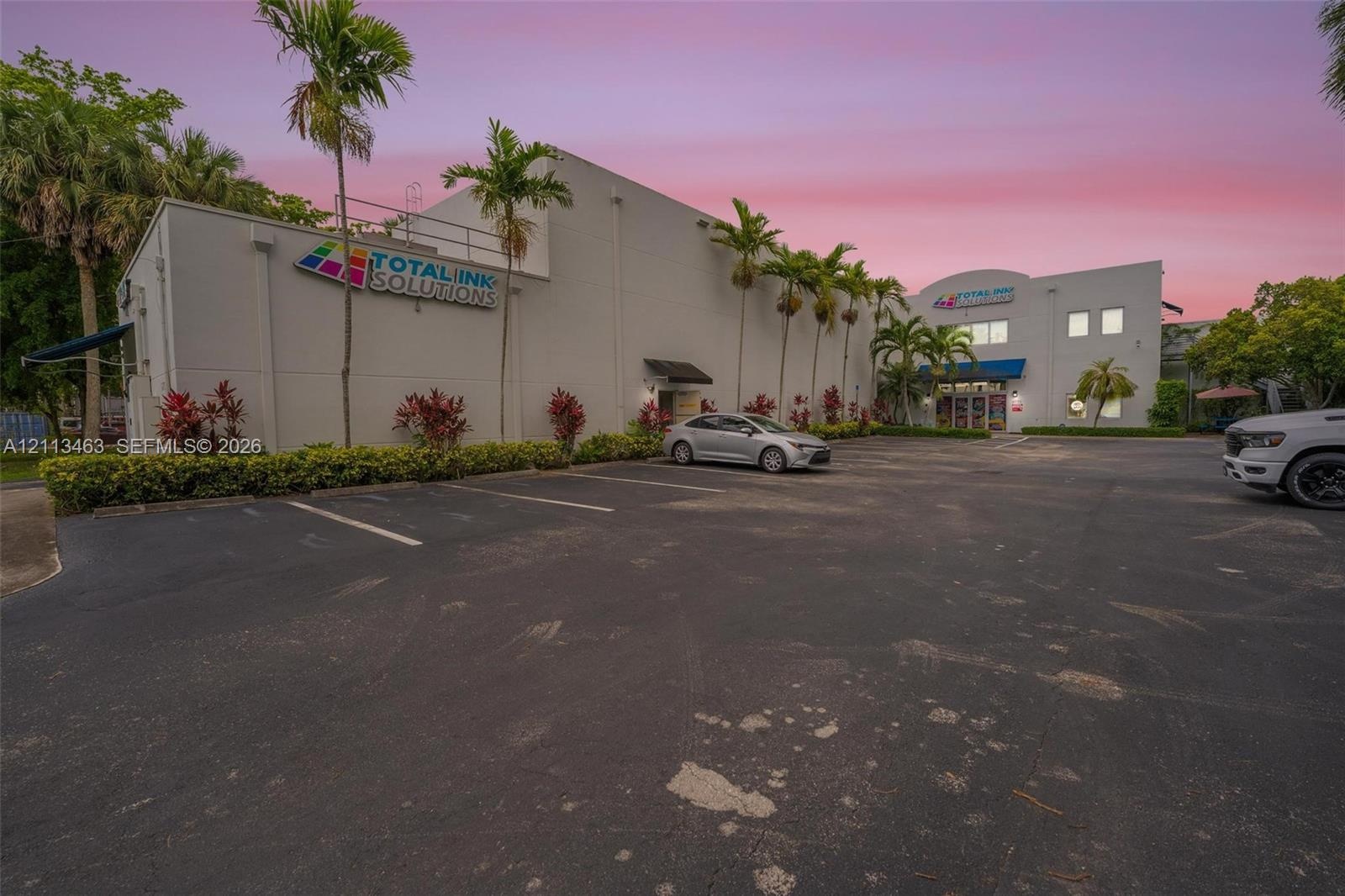 Commercial building featuring concrete exterior walls, paved asphalt parking lot, and manicured landscaping including mature palm trees