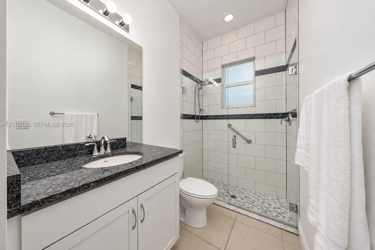 Bathroom featuring a white vanity cabinet with a dark stone countertop, an integrated sink with a chrome faucet, a walk-in shower with a glass enclosu