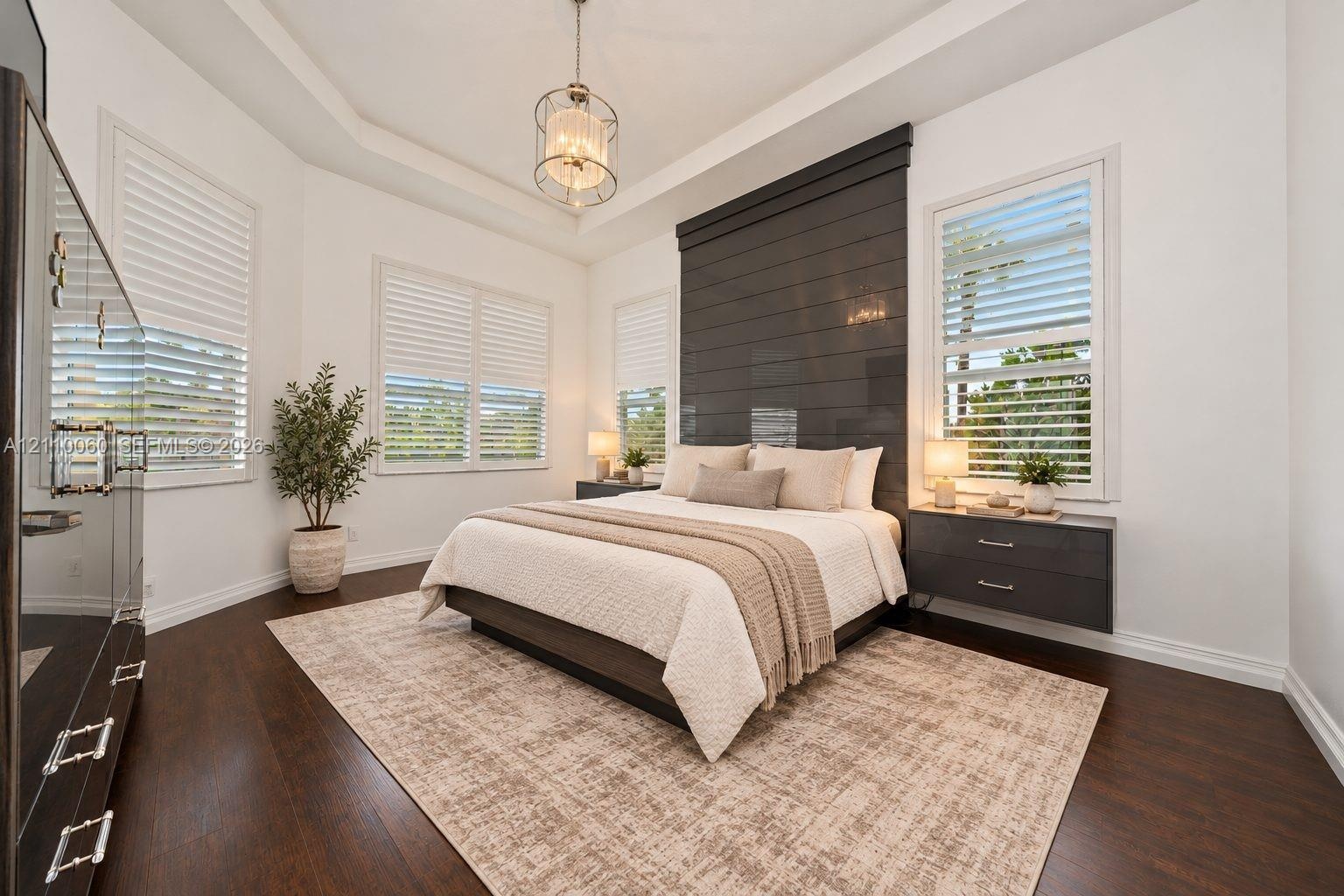 Virtually staged. Tray ceiling with a central pendant light, wood-finish flooring, charcoal horizontal plank accent wall, and dual floating bedside dr