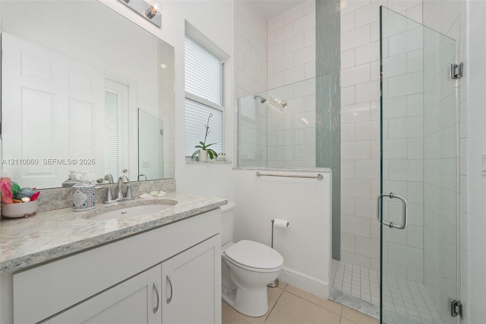 Bathroom featuring a vanity with stone-finish countertop and undermount sink, large wall-mounted mirror, walk-in shower with glass enclosure, vertical