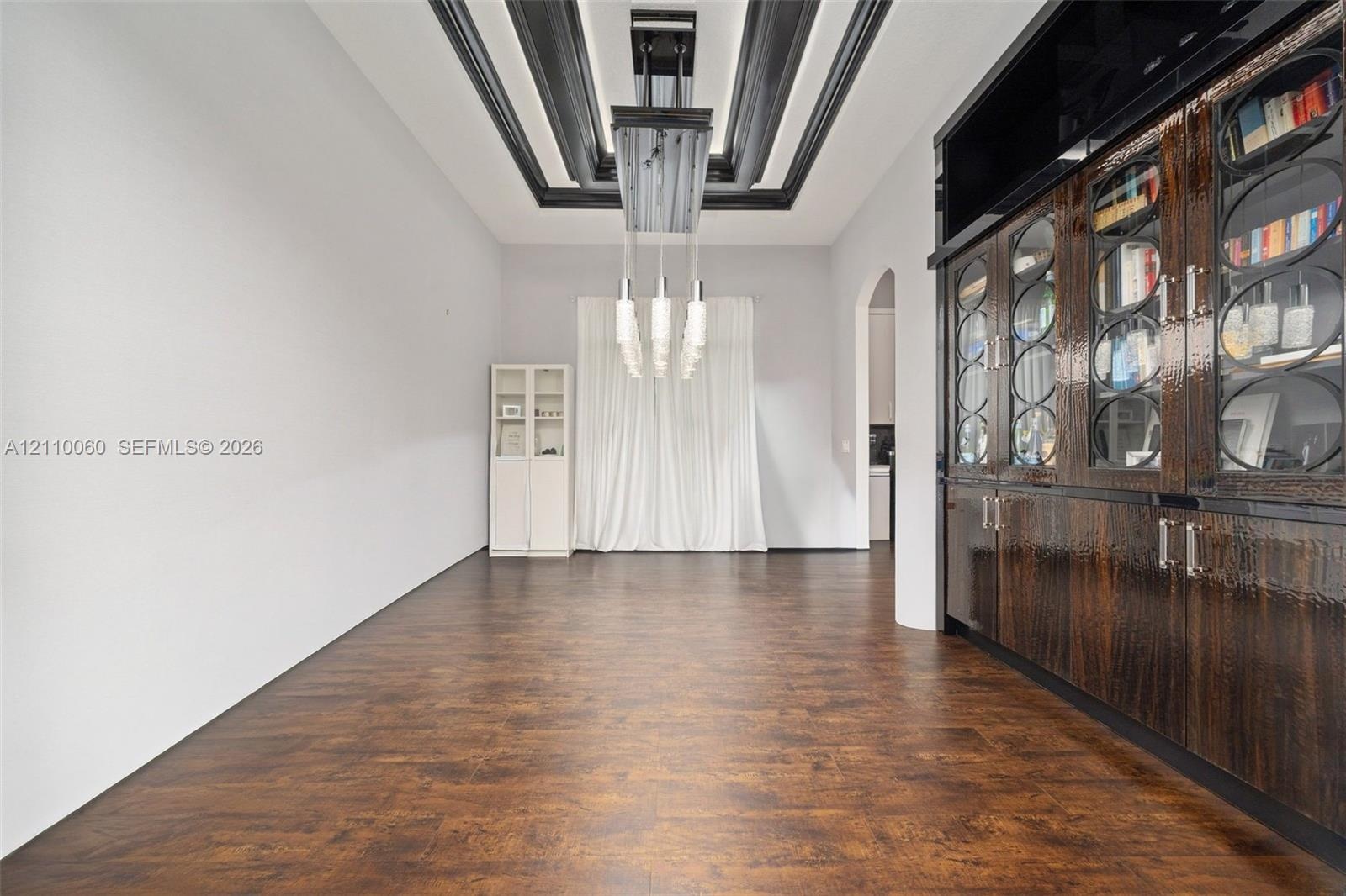 Wood-finish flooring, dramatic coffered ceiling with black detailing, built-in floor-to-ceiling cabinetry with glass-panel doors, and an elongated mul