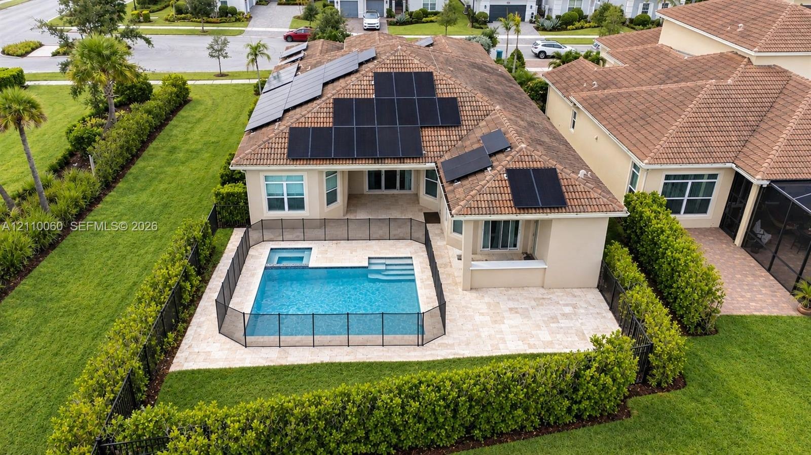 Aerial view of a residential property featuring a tiled roof equipped with integrated solar panels, a private swimming pool with a built-in spa, and a