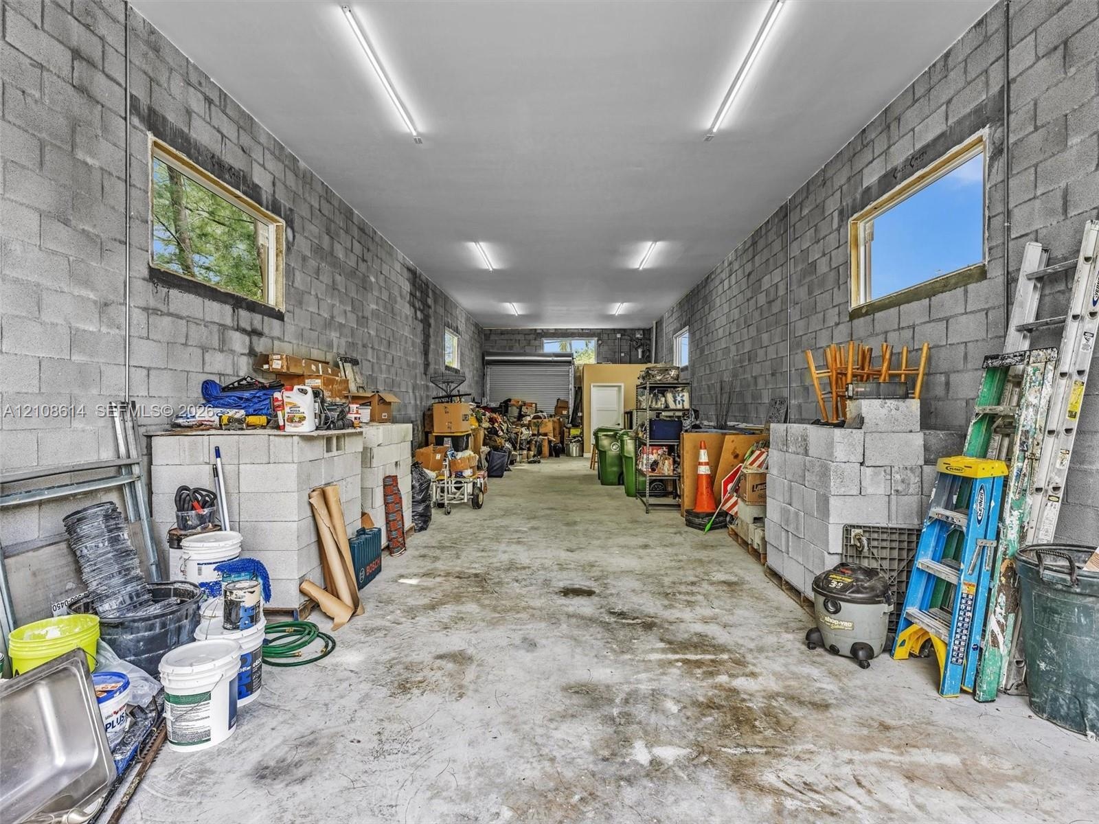 Spacious garage featuring exposed concrete block walls, high-clearance ceilings, concrete flooring, multiple horizontal-slider windows, and linear LED