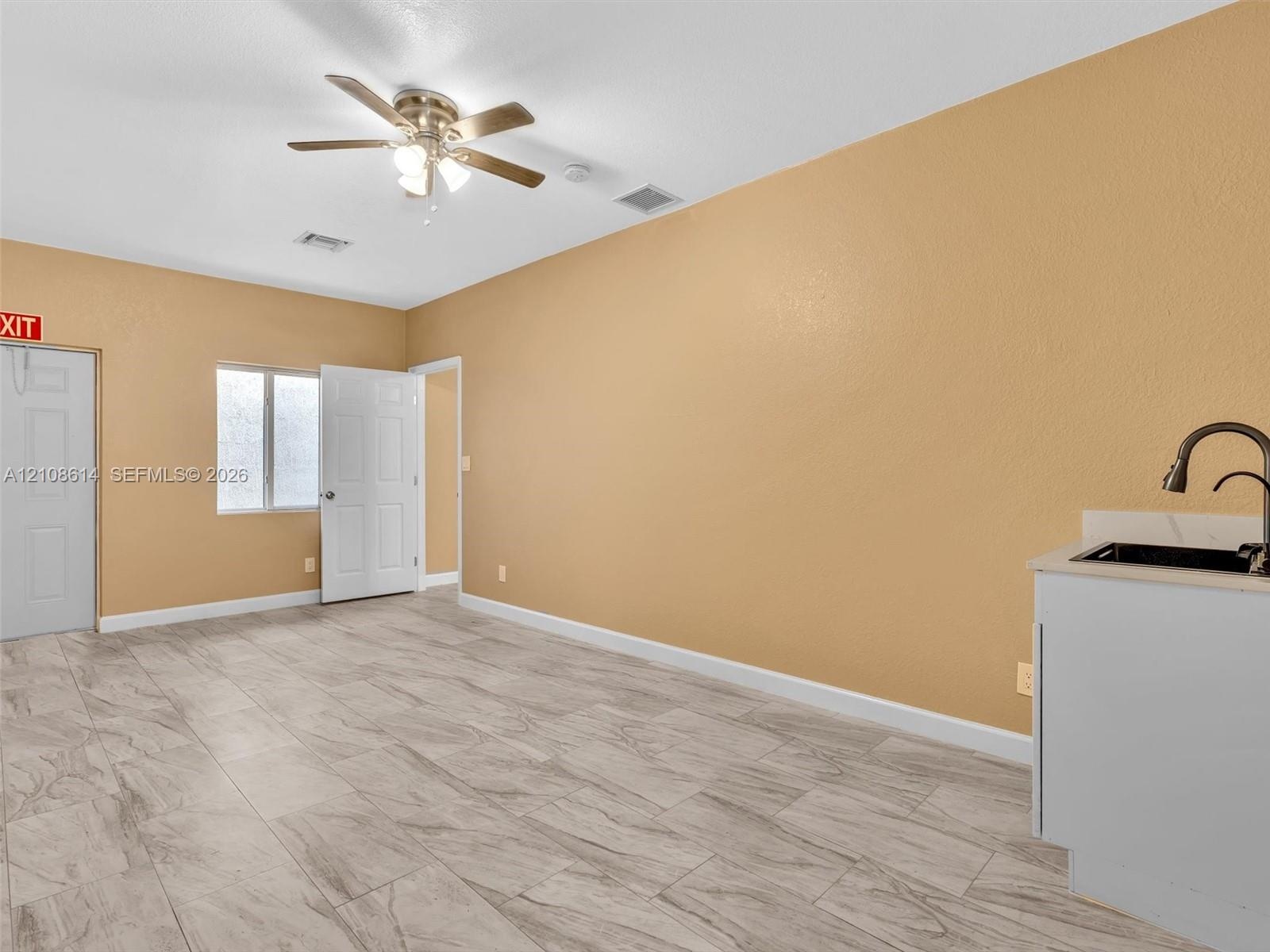 Tile flooring with a wood-grain finish, white cabinetry with a light-toned countertop, integrated sink with a gooseneck faucet, ceiling fan, and windo