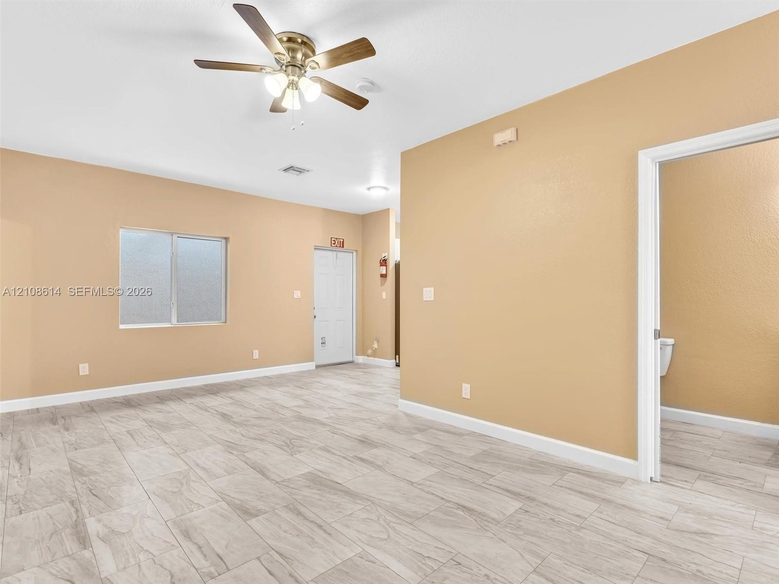 Neutral-toned interior featuring wood-finish tile flooring, a multi-blade ceiling fan with integrated light fixture, and a single-hung window with fro