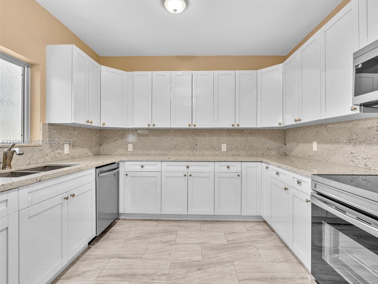 Kitchen featuring white shaker-style cabinetry, stone countertops, integrated stainless steel appliances, and large-format tile flooring