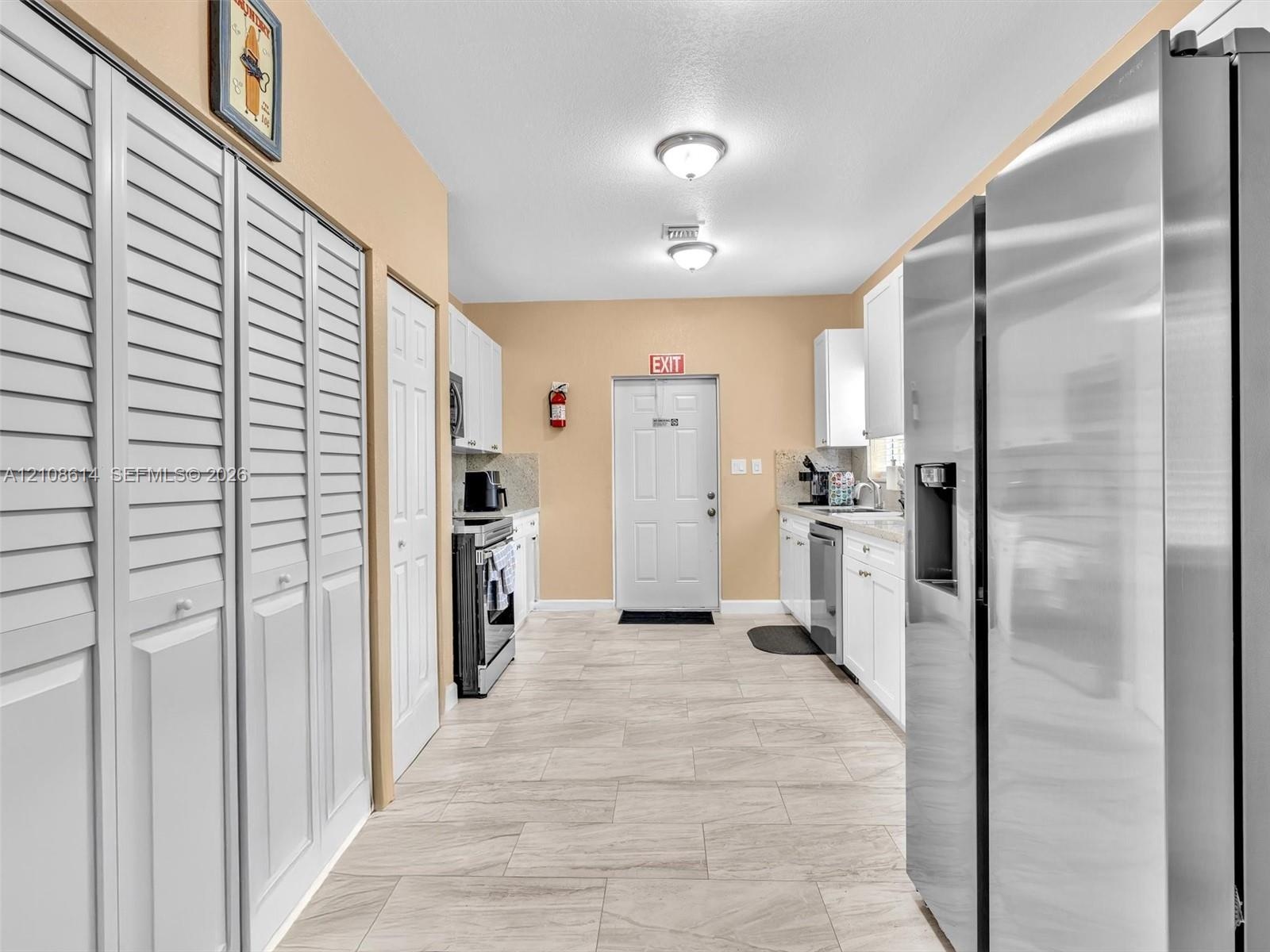 Kitchen featuring white cabinetry, stainless steel appliances, dual ceiling-mounted lighting, and tile flooring with louvered closet doors