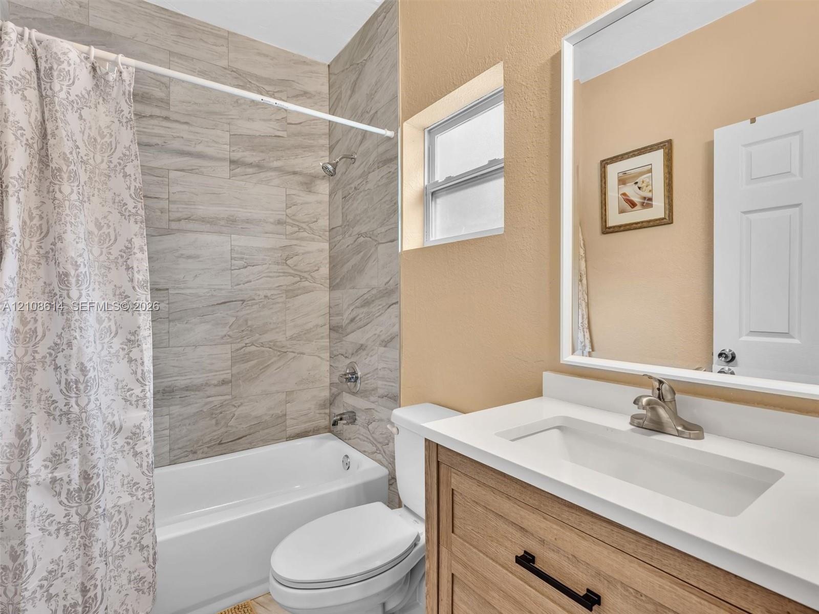 Bathroom featuring a vanity with a light wood finish, white countertop, integrated rectangular sink, and matte black hardware, accompanied by a tub en