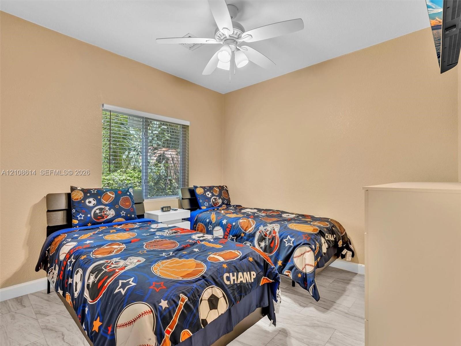 Neutral-toned room featuring a central ceiling fan with integrated lighting, wood-finish flooring, and a window with horizontal blinds