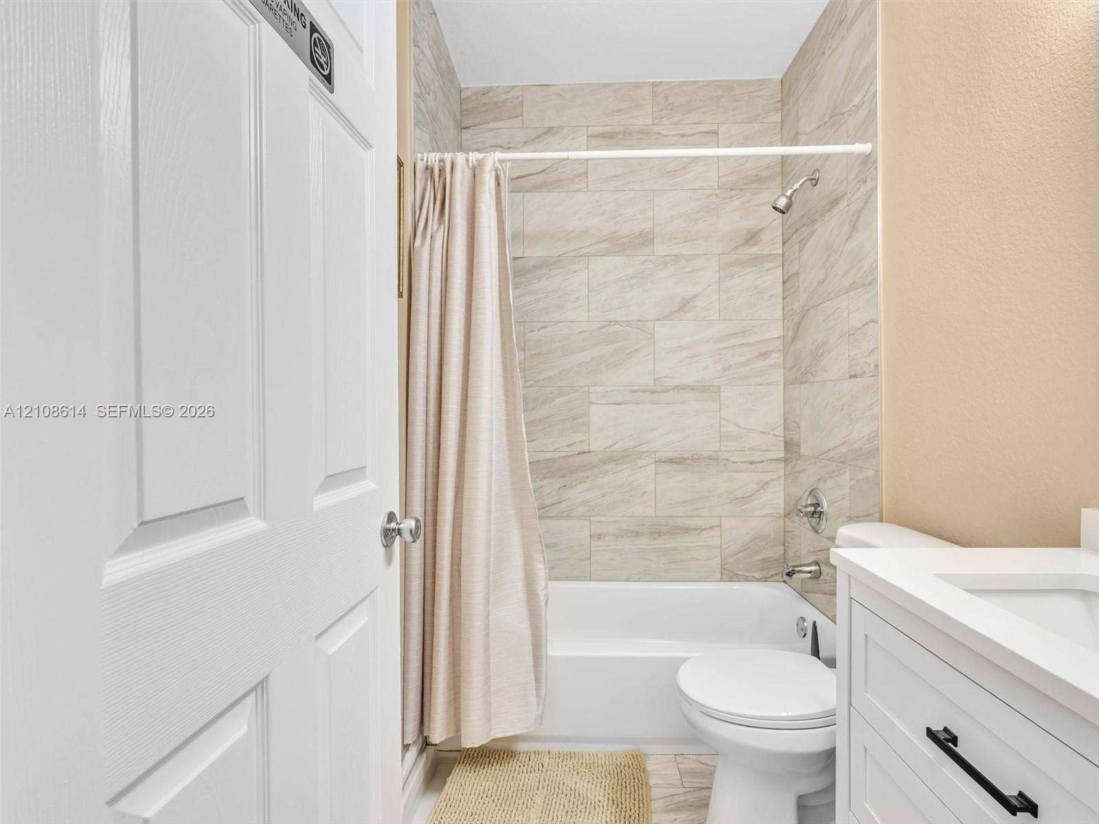 Bathroom featuring a white vanity cabinet with matte black hardware, a porcelain tub, and neutral stone-finish ceramic wall tile