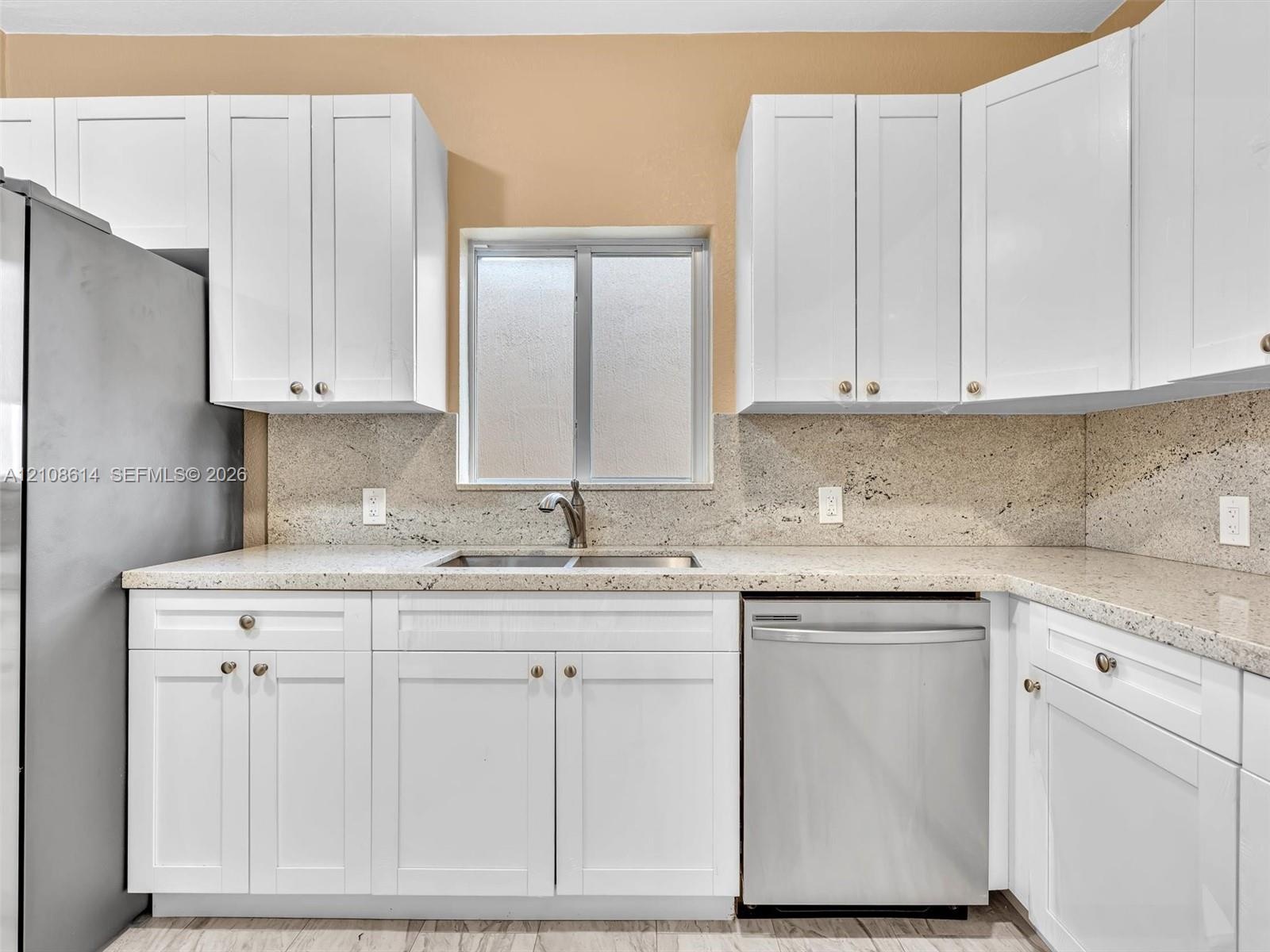 Kitchen featuring white shaker-style cabinetry, stone-surface countertops, stone backsplash, stainless steel dishwasher, and a dual-basin sink with a 