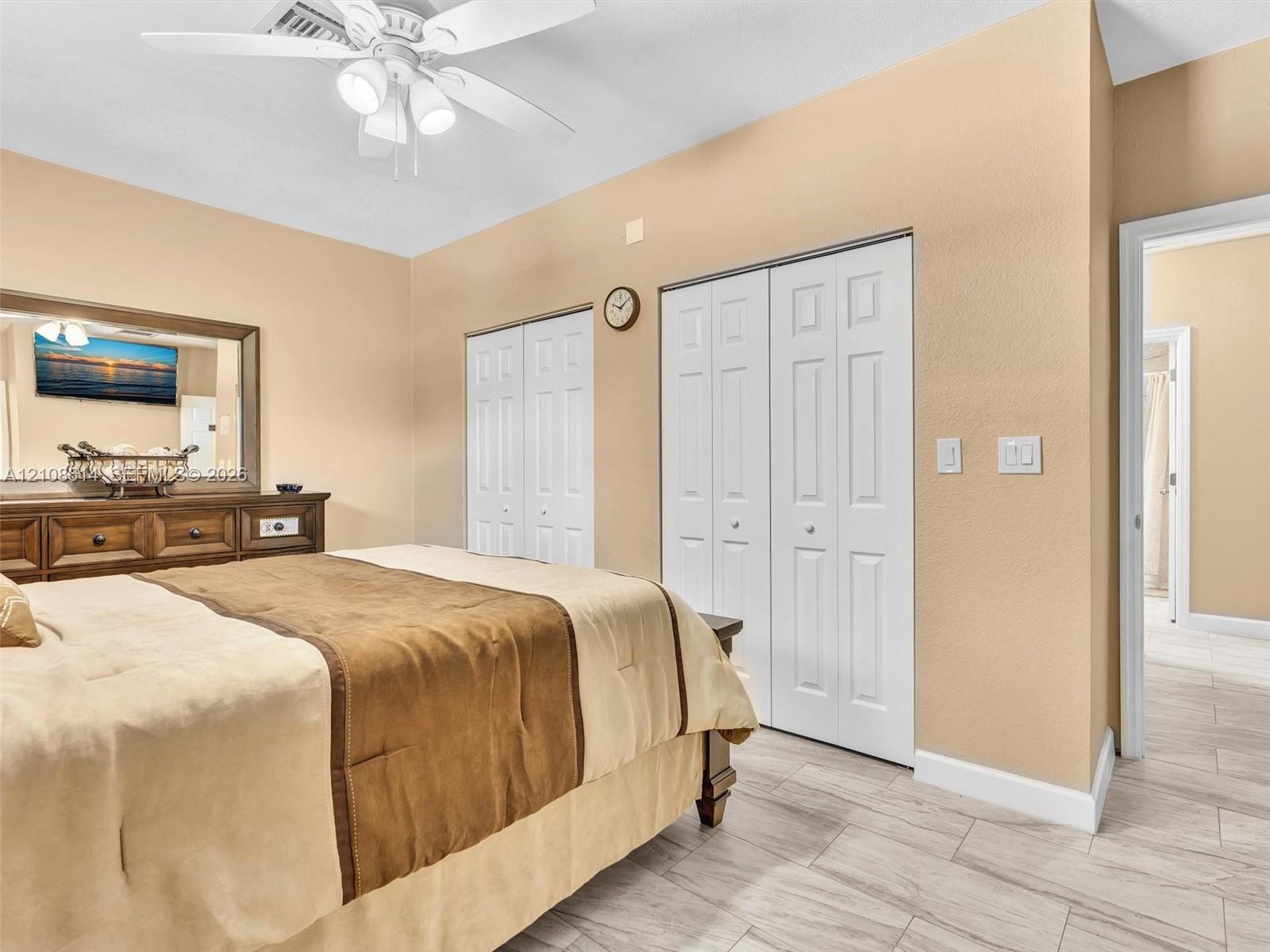 Room featuring wood-finish flooring, dual bi-fold door closets, and a ceiling-mounted fan with integrated lighting