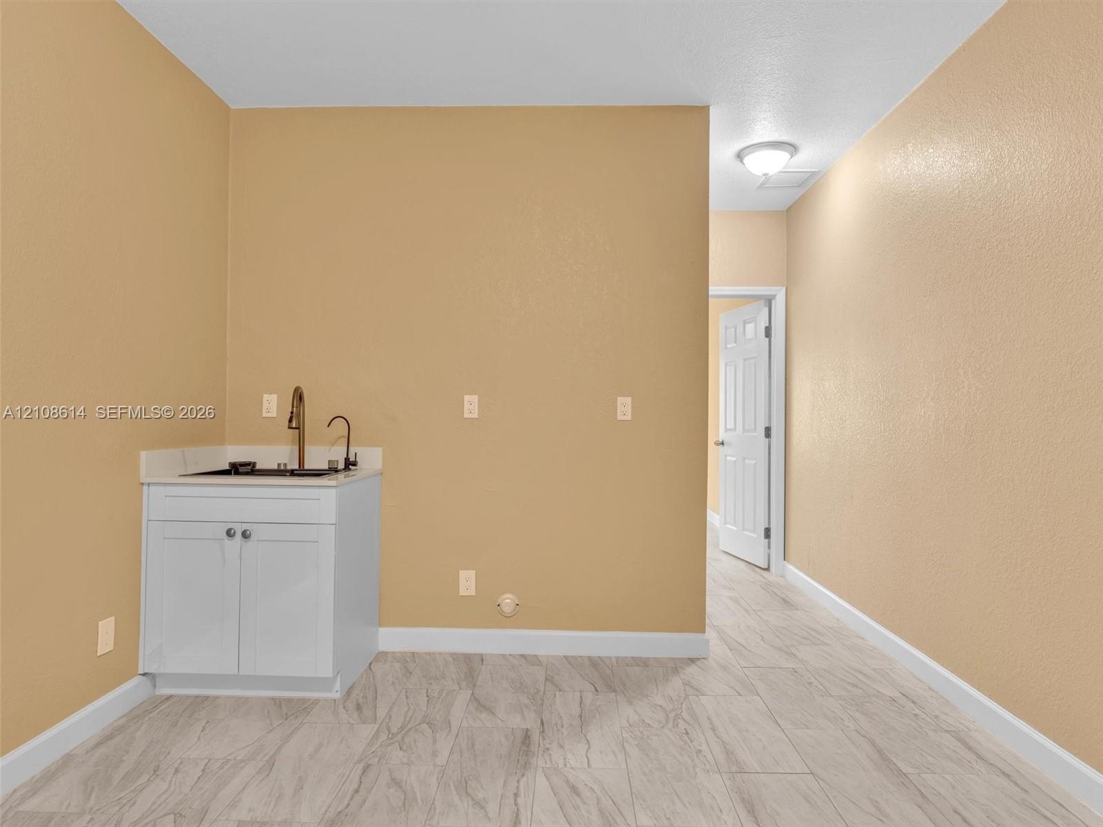 Built-in white vanity featuring a stone countertop, an integrated sink with a tall gooseneck faucet, and light wood-finish flooring