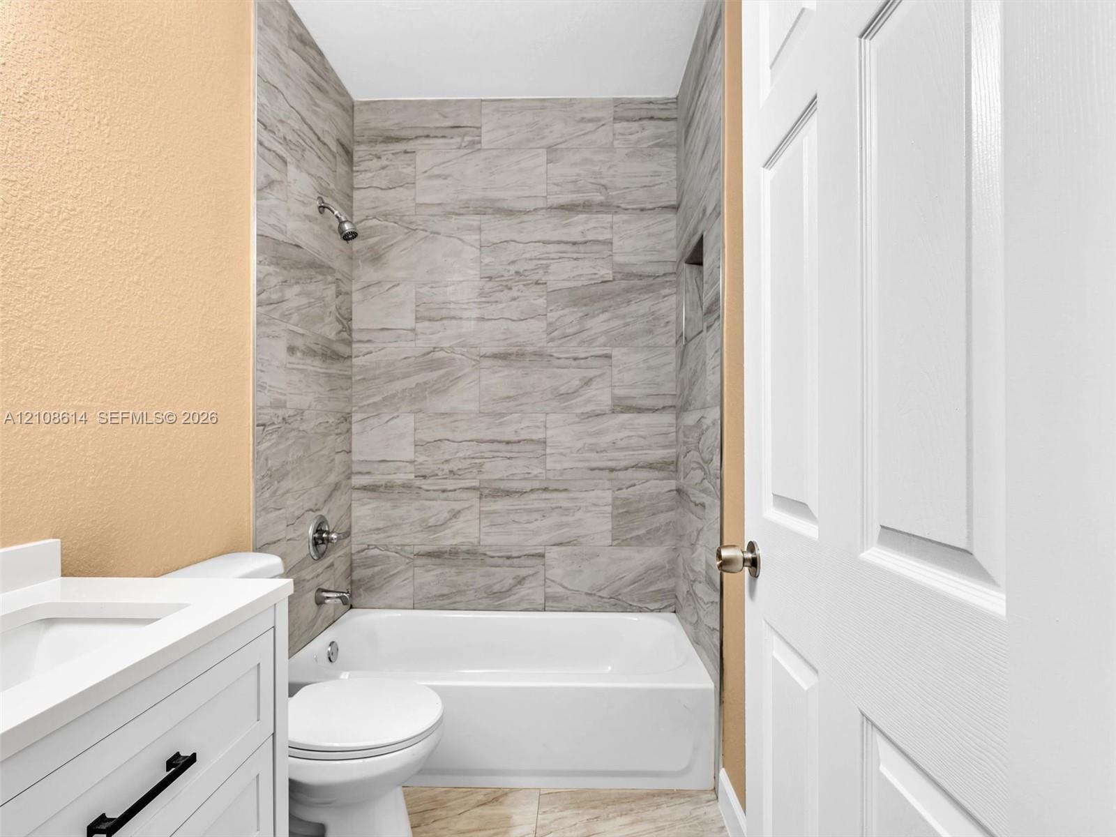 Bathroom featuring a white vanity cabinet with a stone-surface countertop, tub-shower combination with full-height neutral-toned tile surround, built-