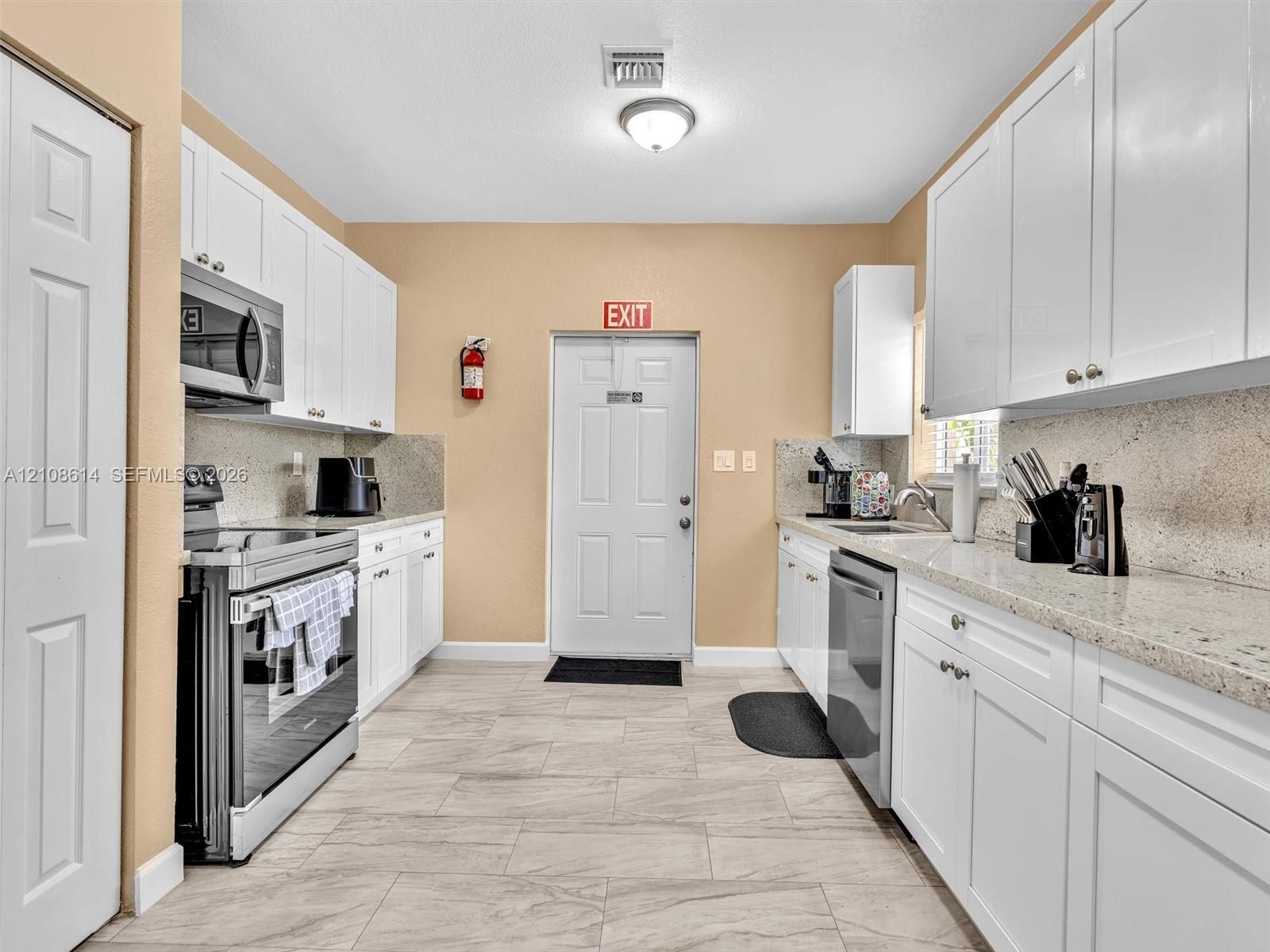 Kitchen featuring white shaker-style cabinetry, stone-finish countertops, stainless steel appliances, and tile flooring