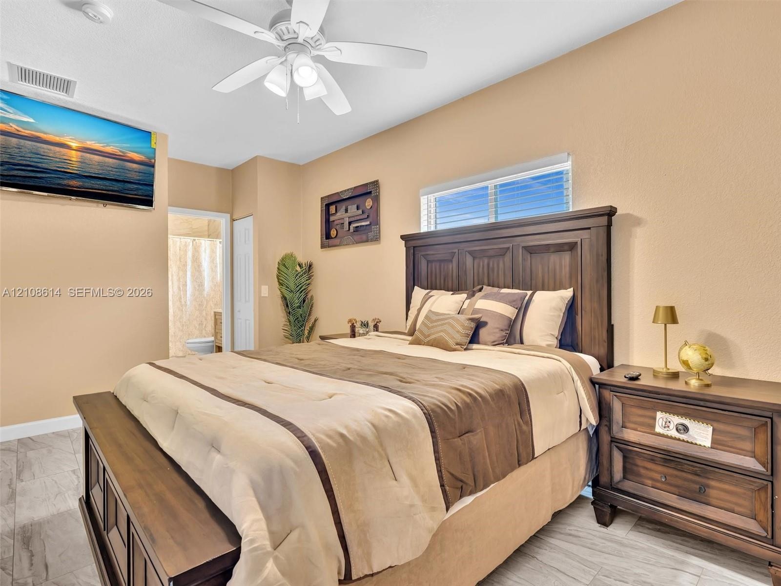 Neutral-toned bedroom featuring tile flooring, horizontal window with integrated blinds, and a ceiling-mounted light fixture with a fan